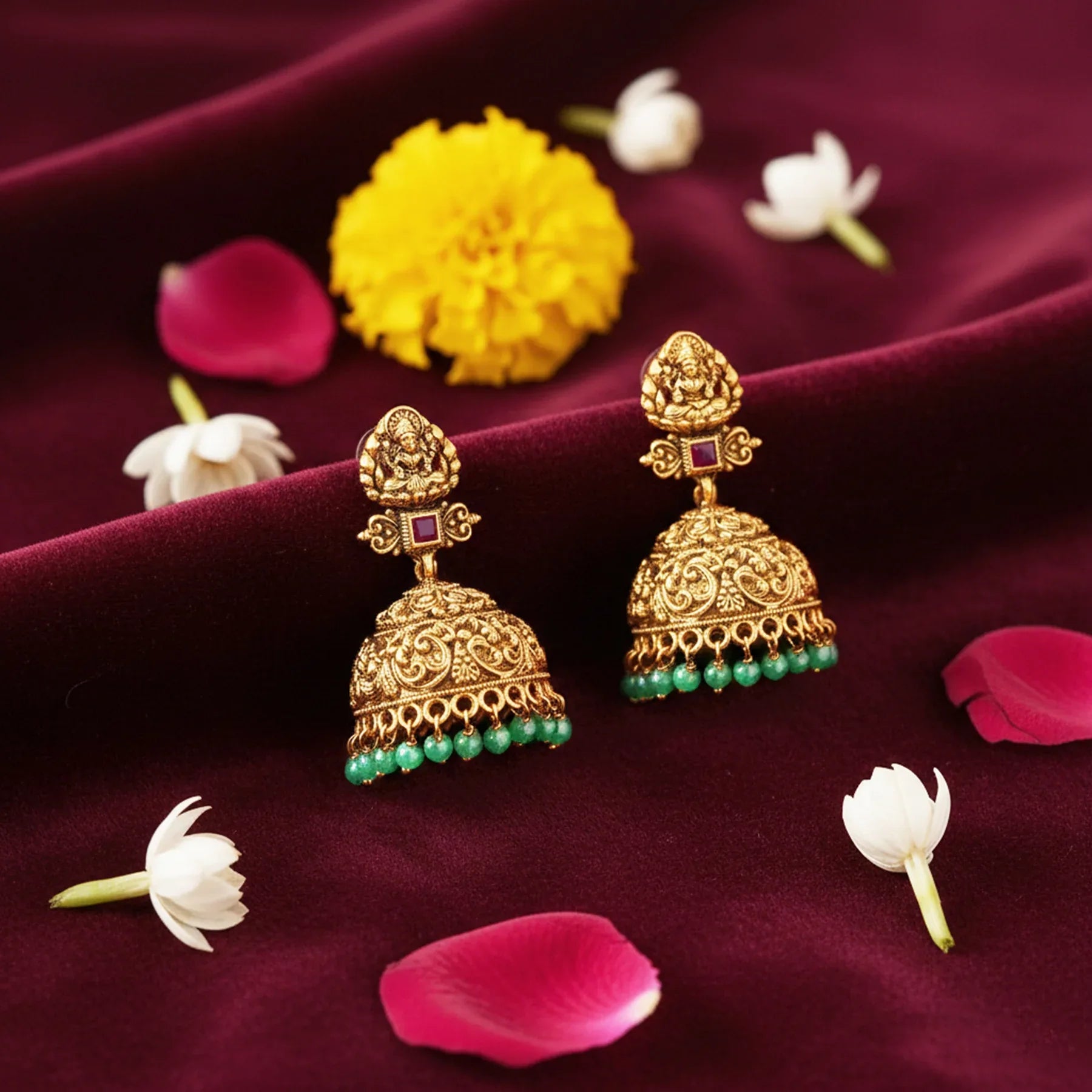 Gold earrings with green gemstones on a purple fabric background with flowers.