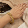 Gold bracelet with gemstones on a hand against a beige fabric background