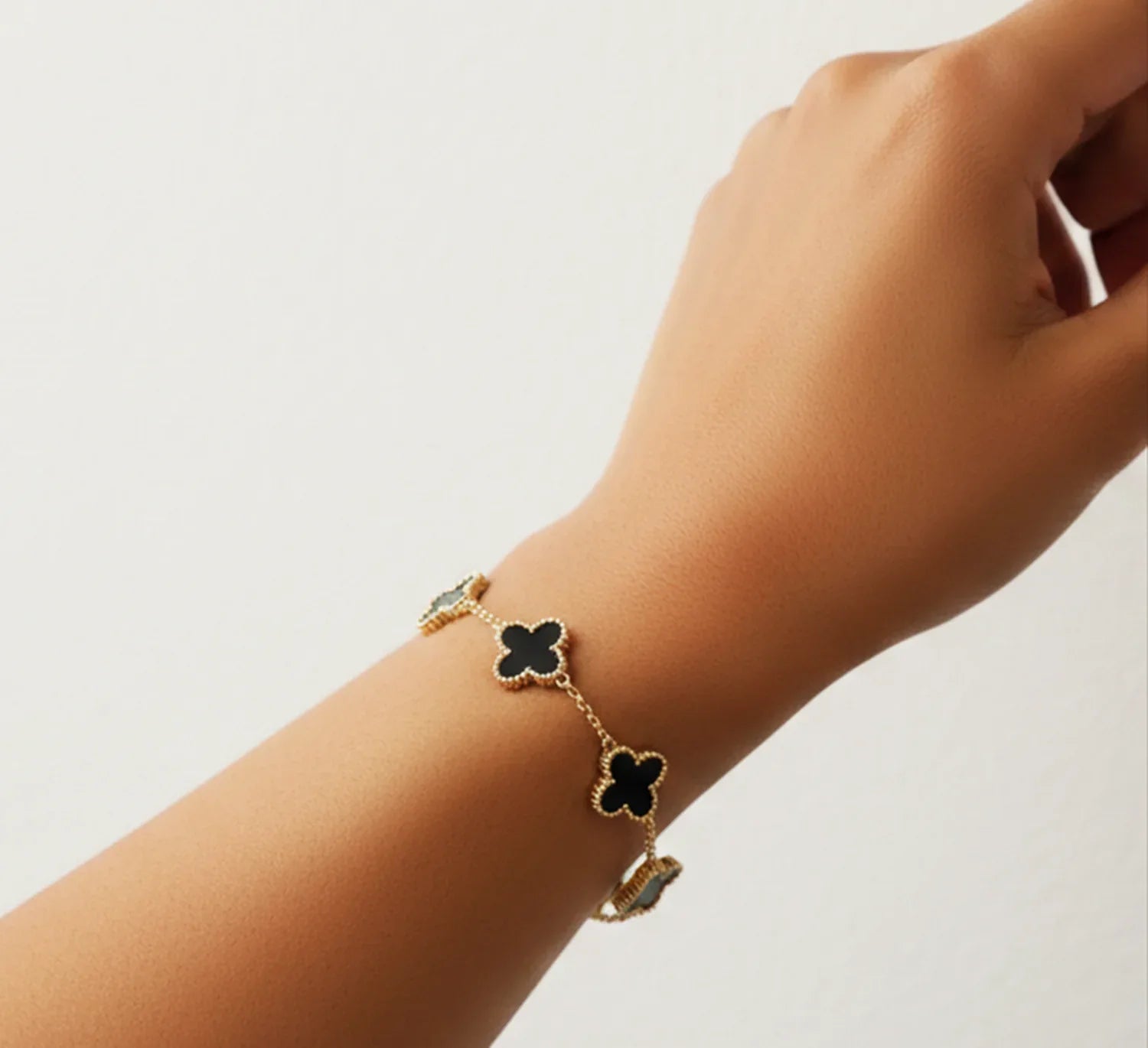 Gold bracelet with black clover charms on a wrist against a light background