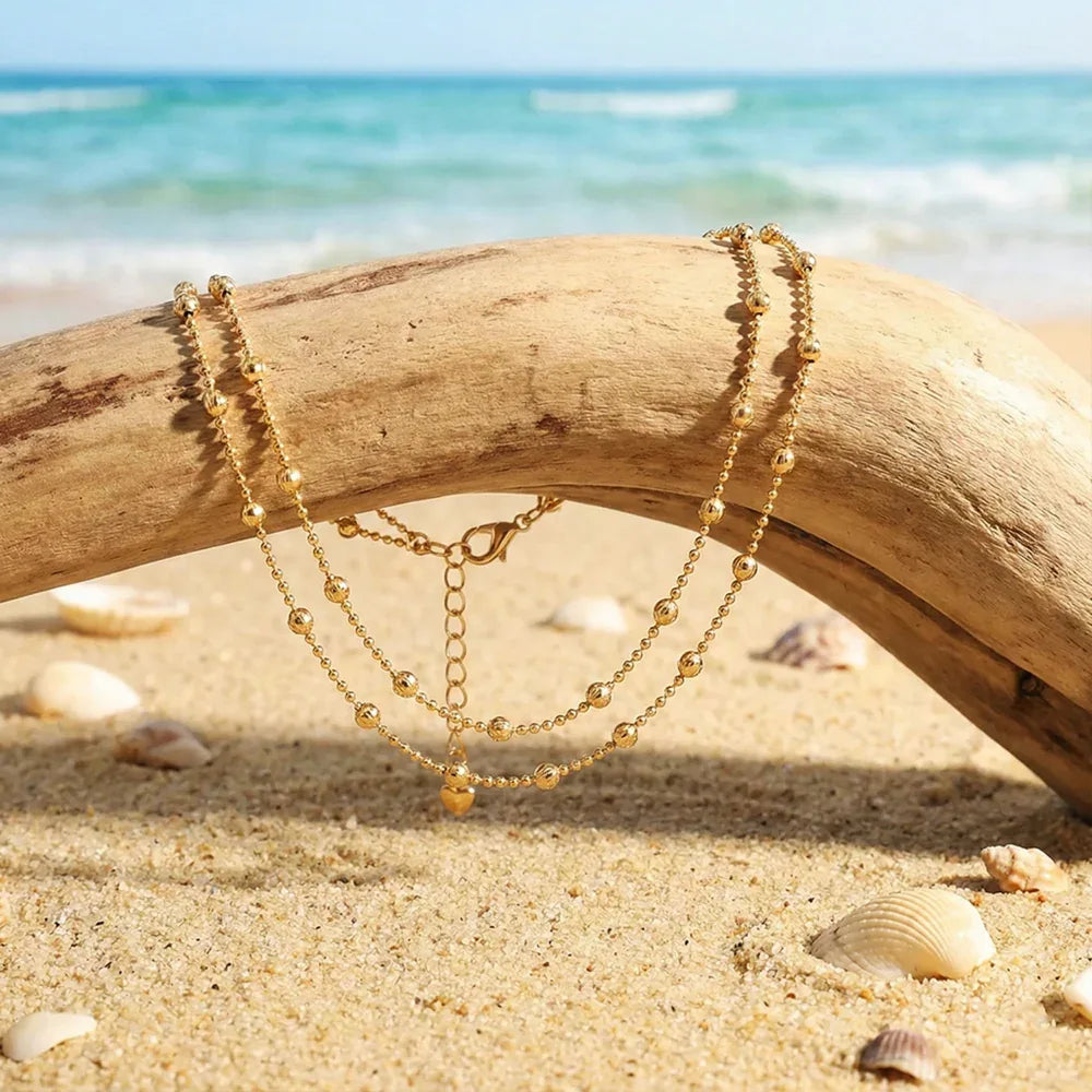 Gold chain necklaces on a piece of driftwood with a beach background