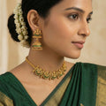 Woman wearing gold jewelry with a green saree against a beige background