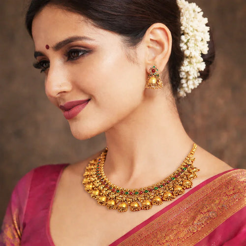 Woman wearing traditional gold jewelry with a pink saree against a brown background