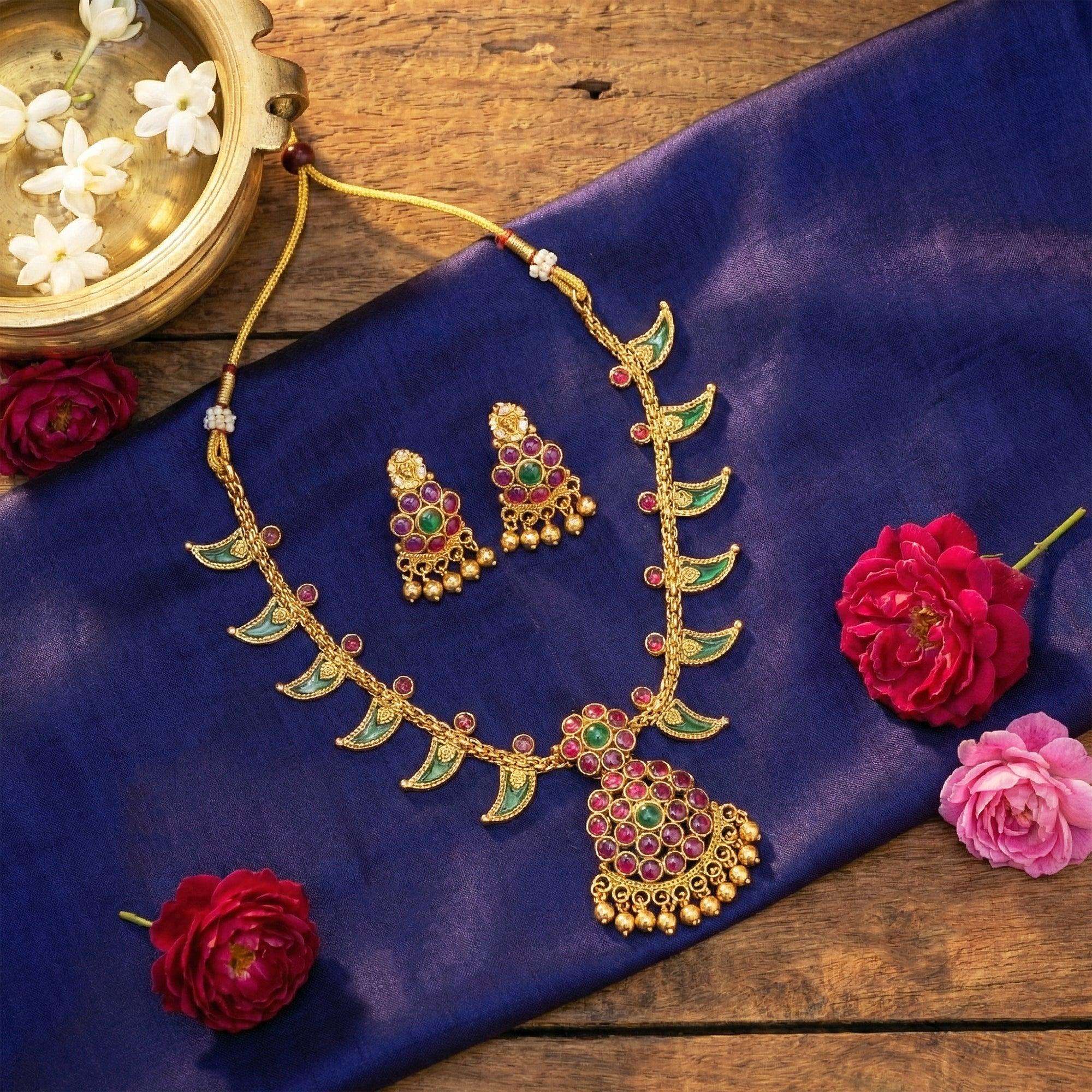 Gold necklace with green and red stones on a blue fabric with flowers