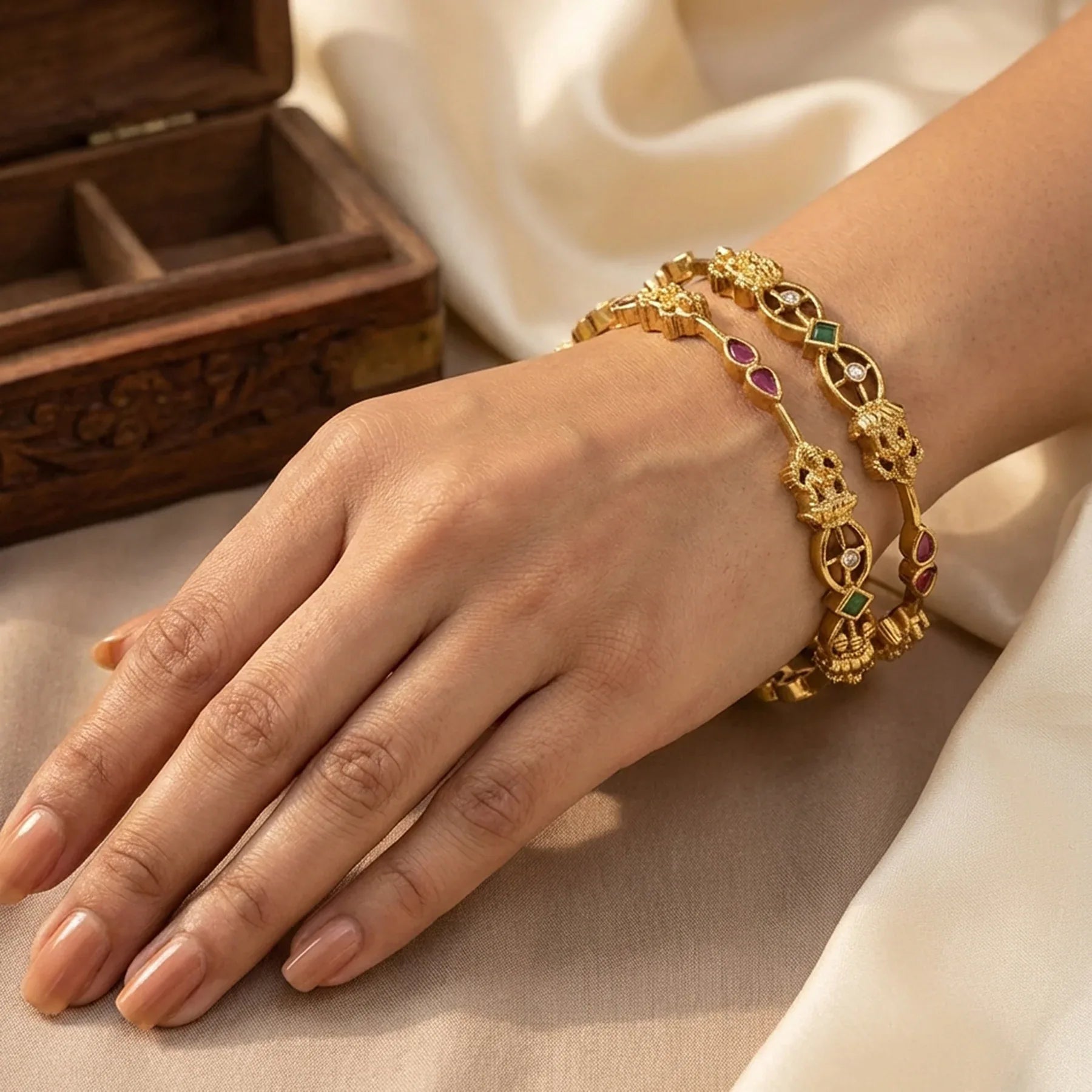 Gold bracelet with gemstones on a hand, wooden box in the background