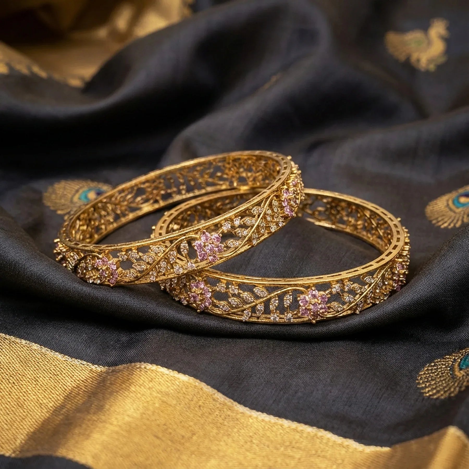 Gold bangles with gemstones on a black and gold fabric background