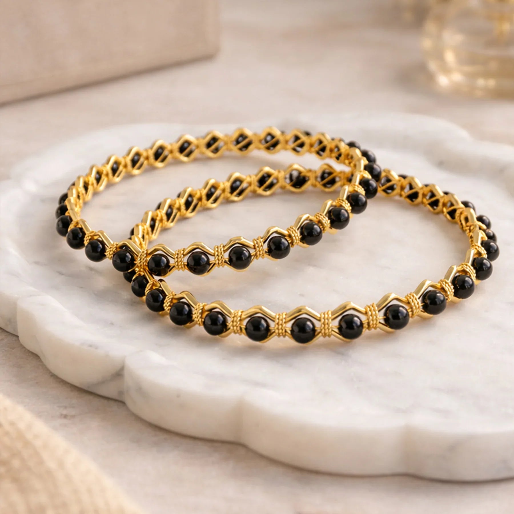 Two gold and black beaded bracelets on a marble surface