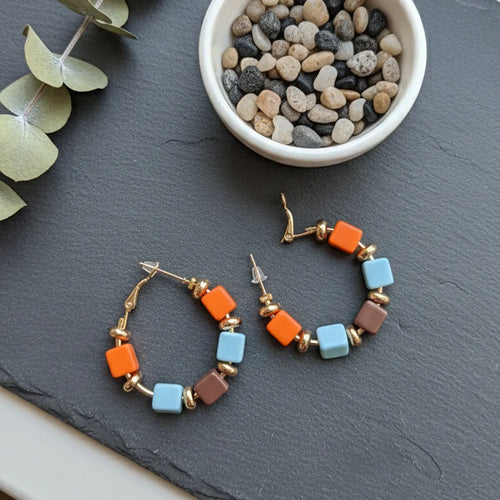 Colorful hoop earrings on a dark surface with pebbles and eucalyptus leaves.