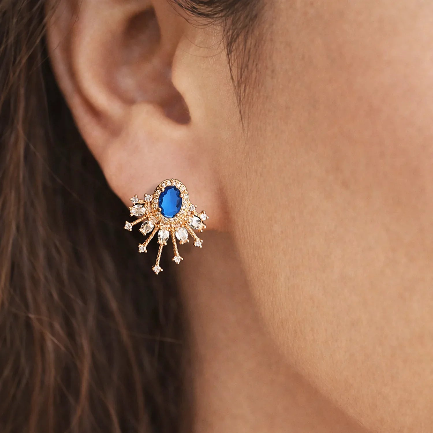 Close-up of an ear wearing a gold earring with a blue gemstone.