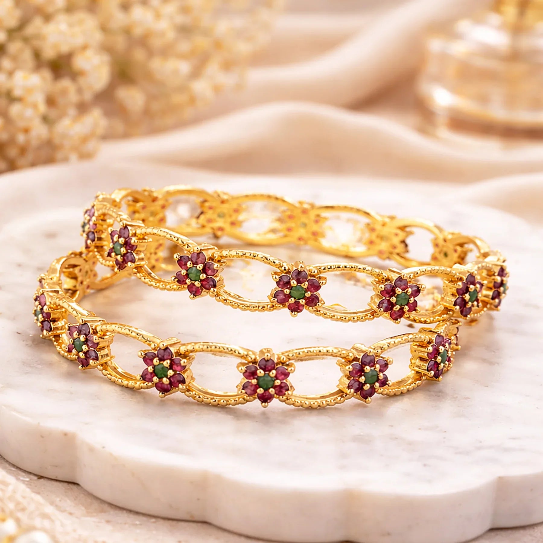 Gold bracelet with red and green gemstones on a beige fabric background