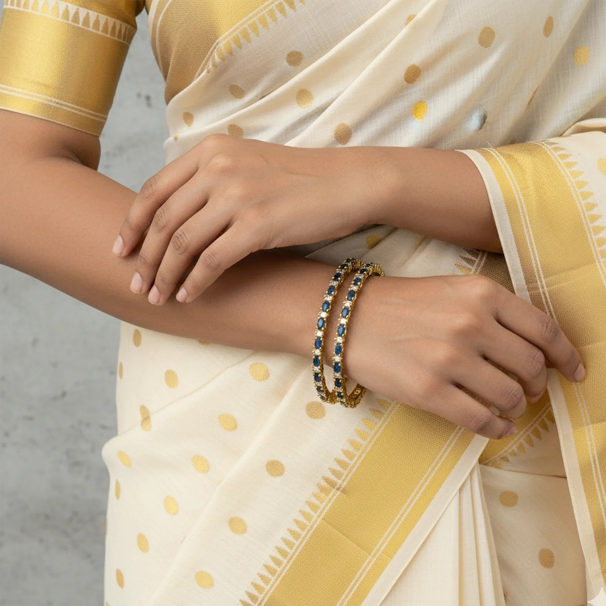 Person wearing a cream saree with gold polka dots and gold jewelry.