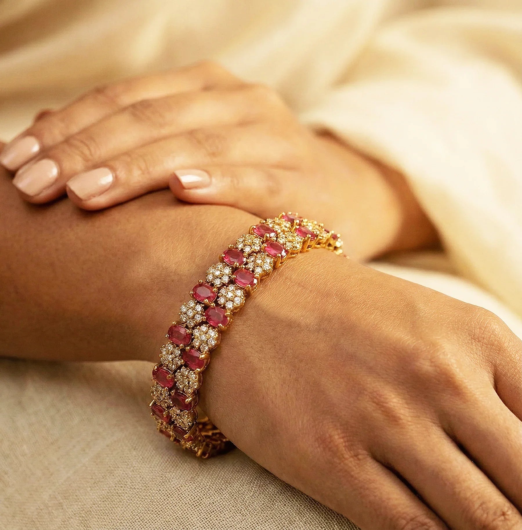 Gold bracelet with red gemstones on a person's wrist against a beige fabric background