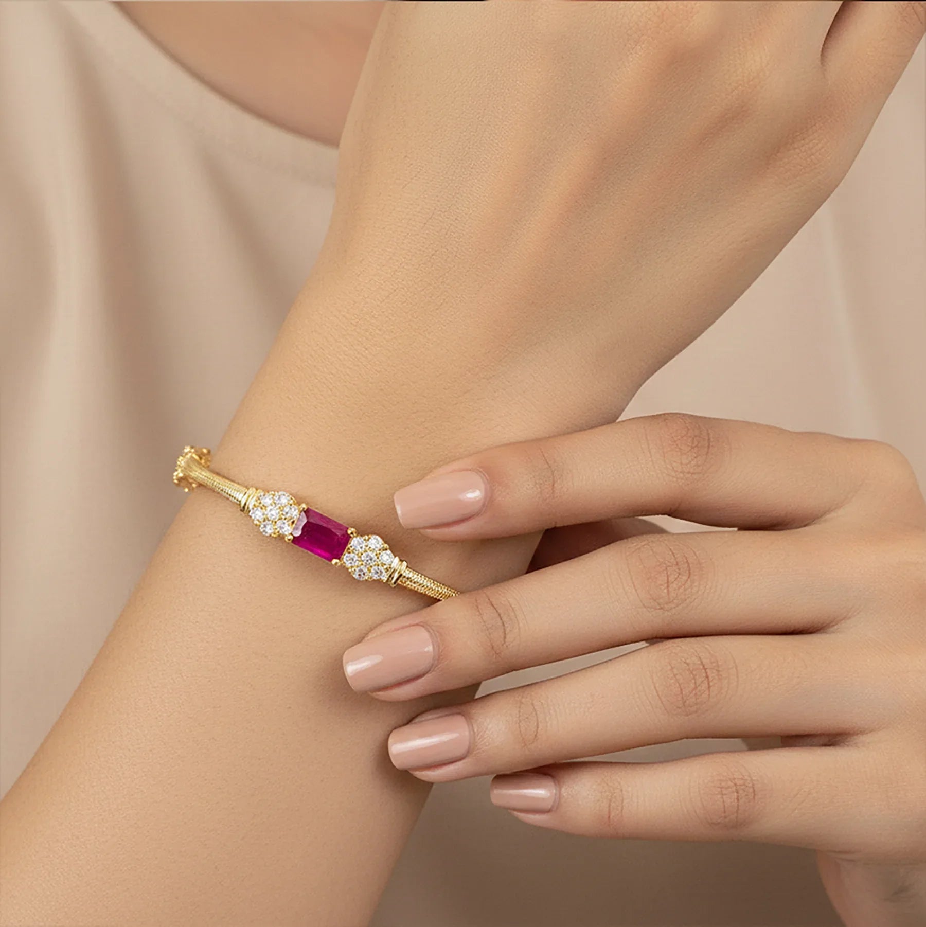 Gold bracelet with a red gemstone on a wrist against a beige background