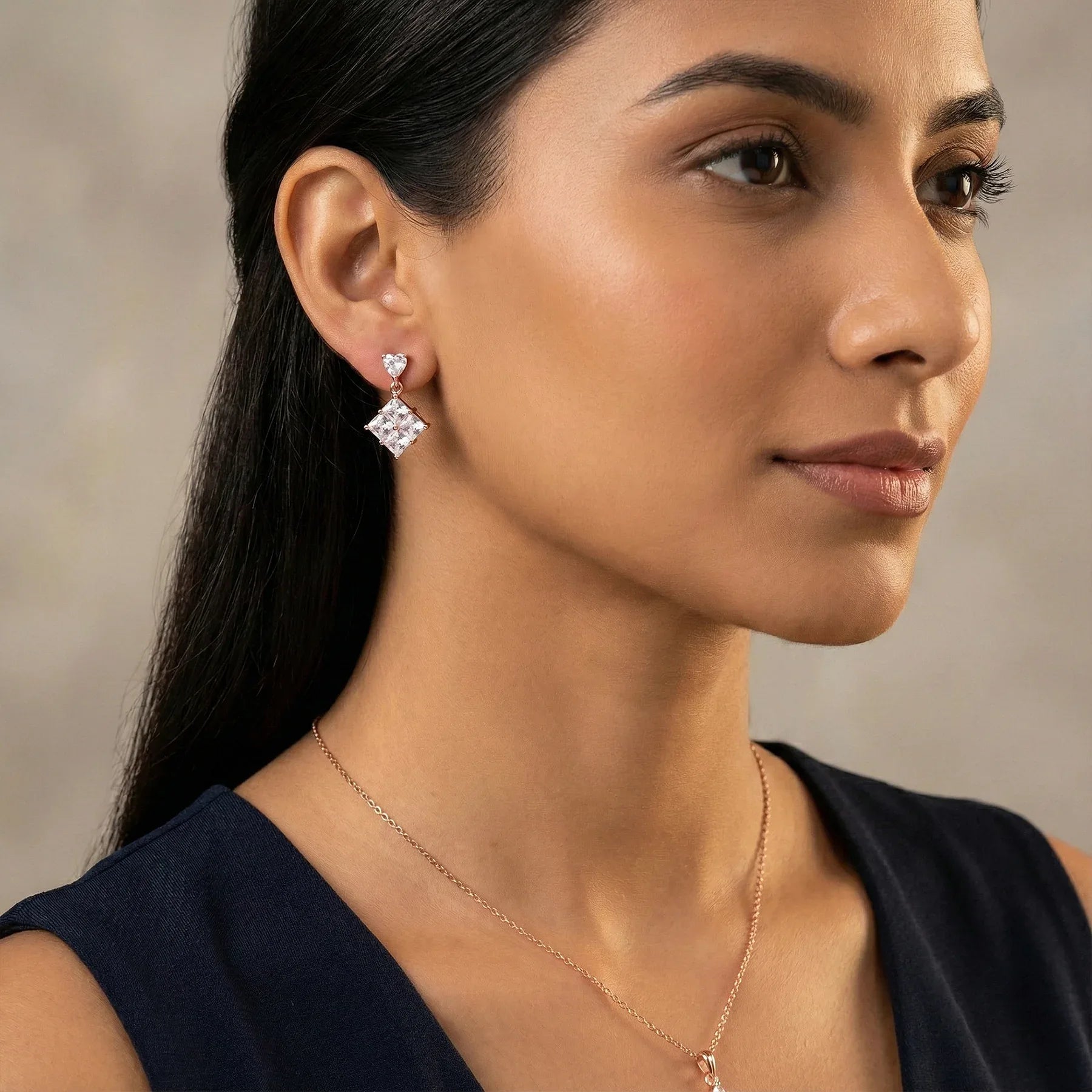 Close-up of a woman wearing diamond earrings and a necklace against a neutral background