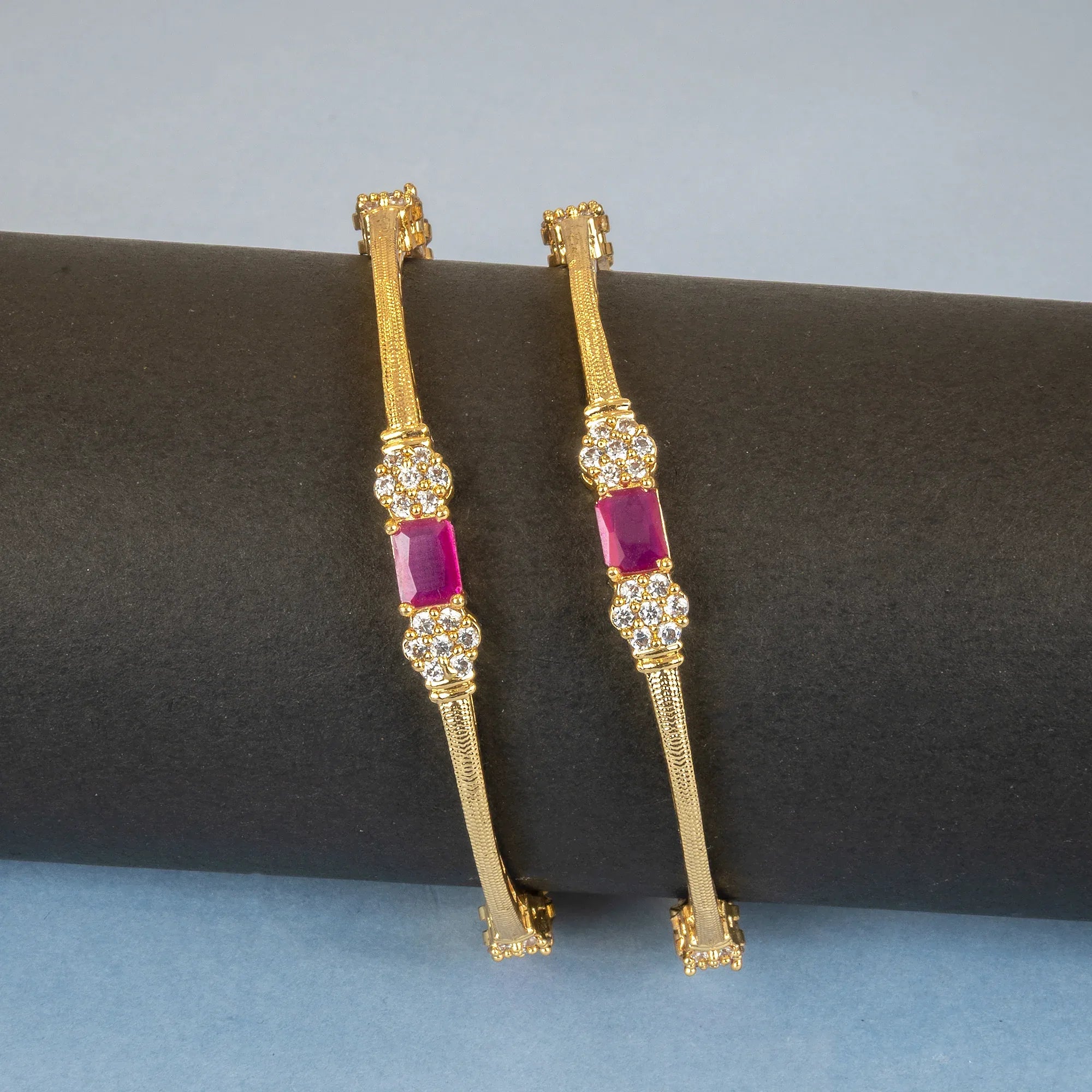 Gold earrings with red gemstones on a black cushion against a blue background