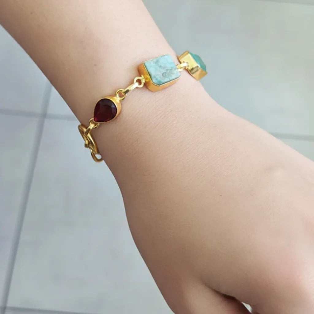 Gold bracelet with turquoise and red stones on a wrist against a neutral background