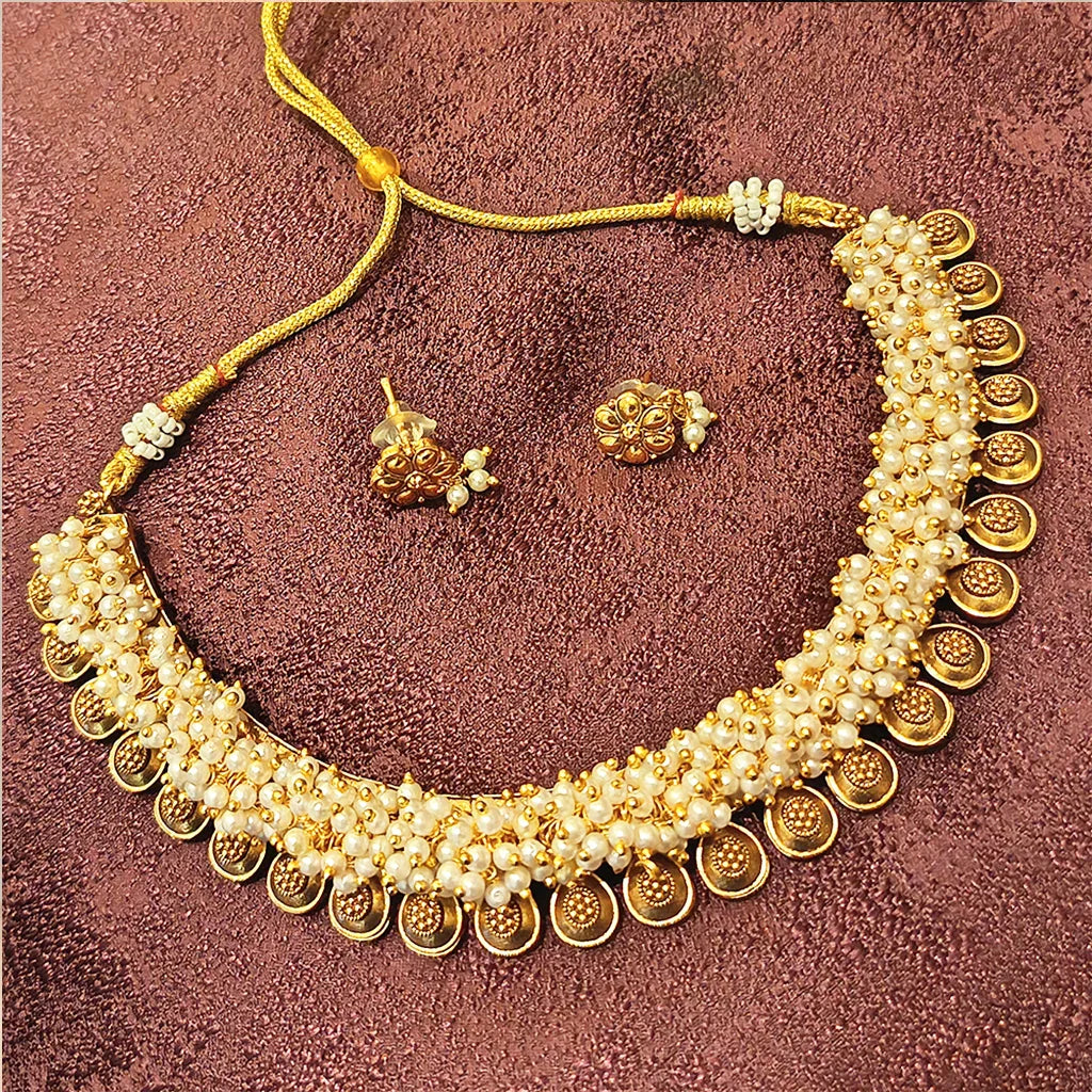Gold necklace with pearl accents and matching earrings on a textured brown background