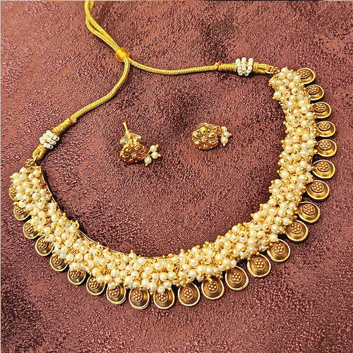 Gold necklace with pearl accents and matching earrings on a textured brown background