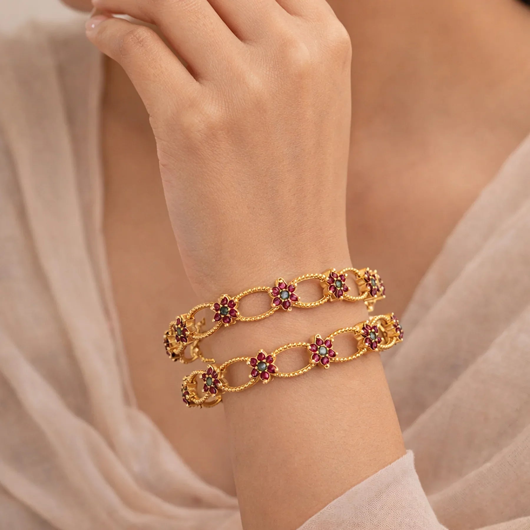 Gold bracelet with floral designs and gemstones on a wrist against a neutral background