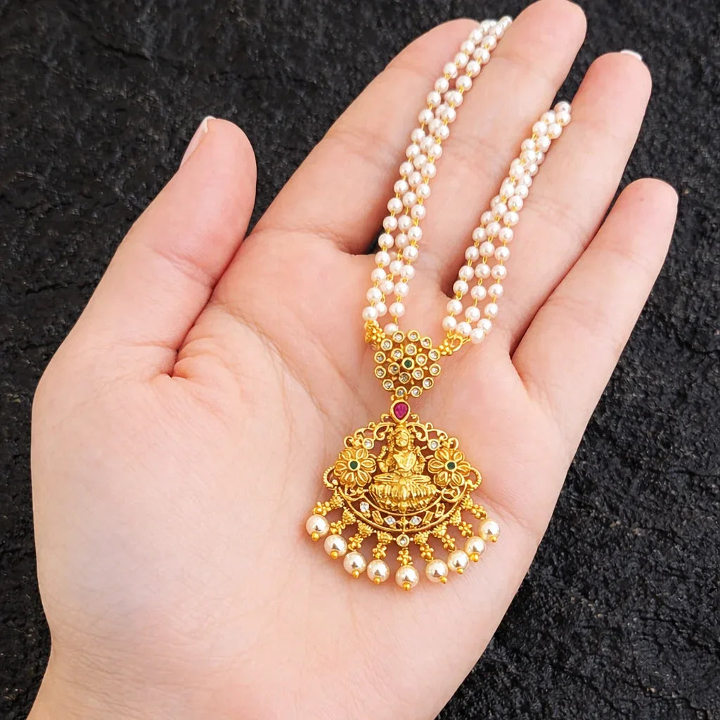 Gold necklace with a large pendant held in a hand against a black background