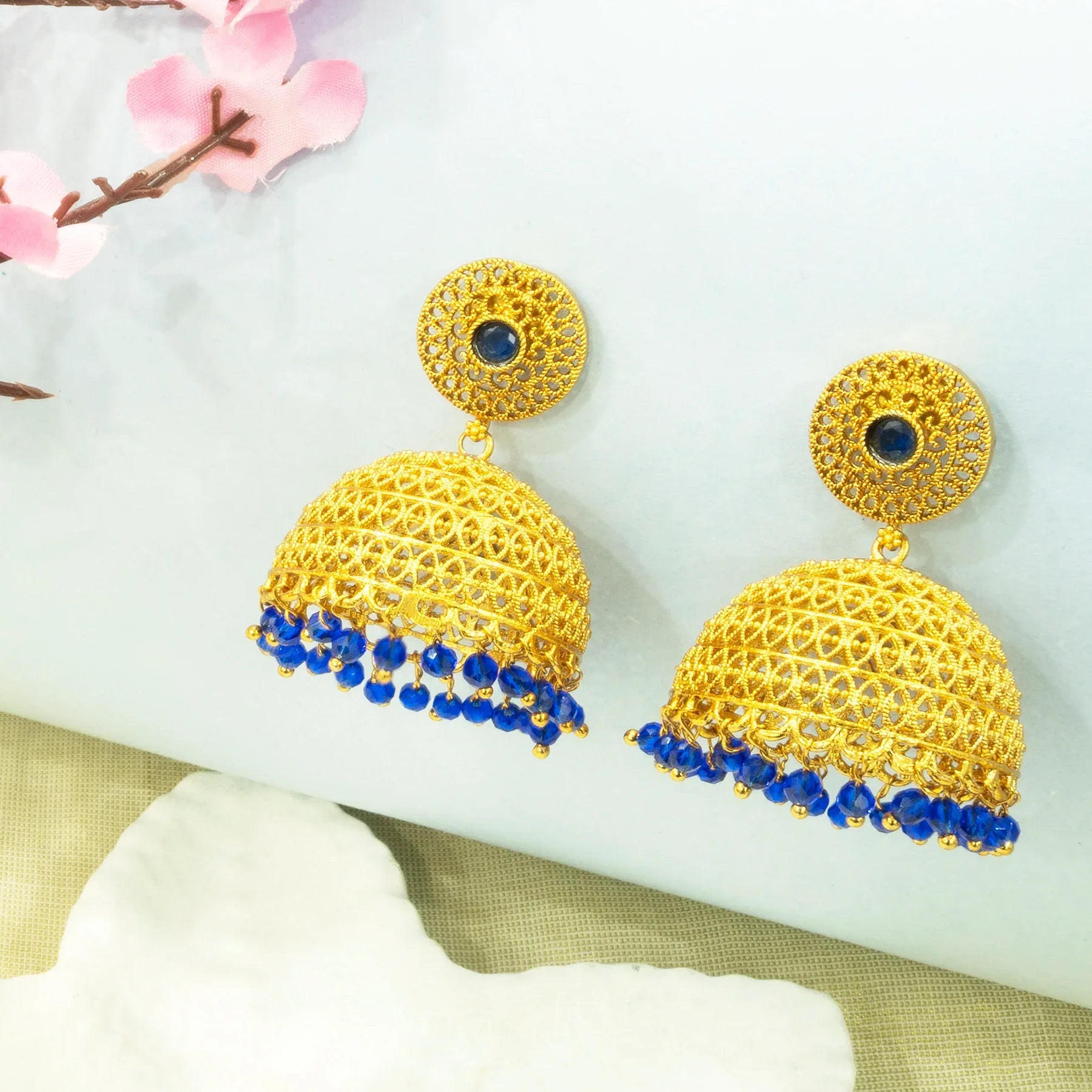Gold earrings with blue beads on a white surface with pink flowers.
