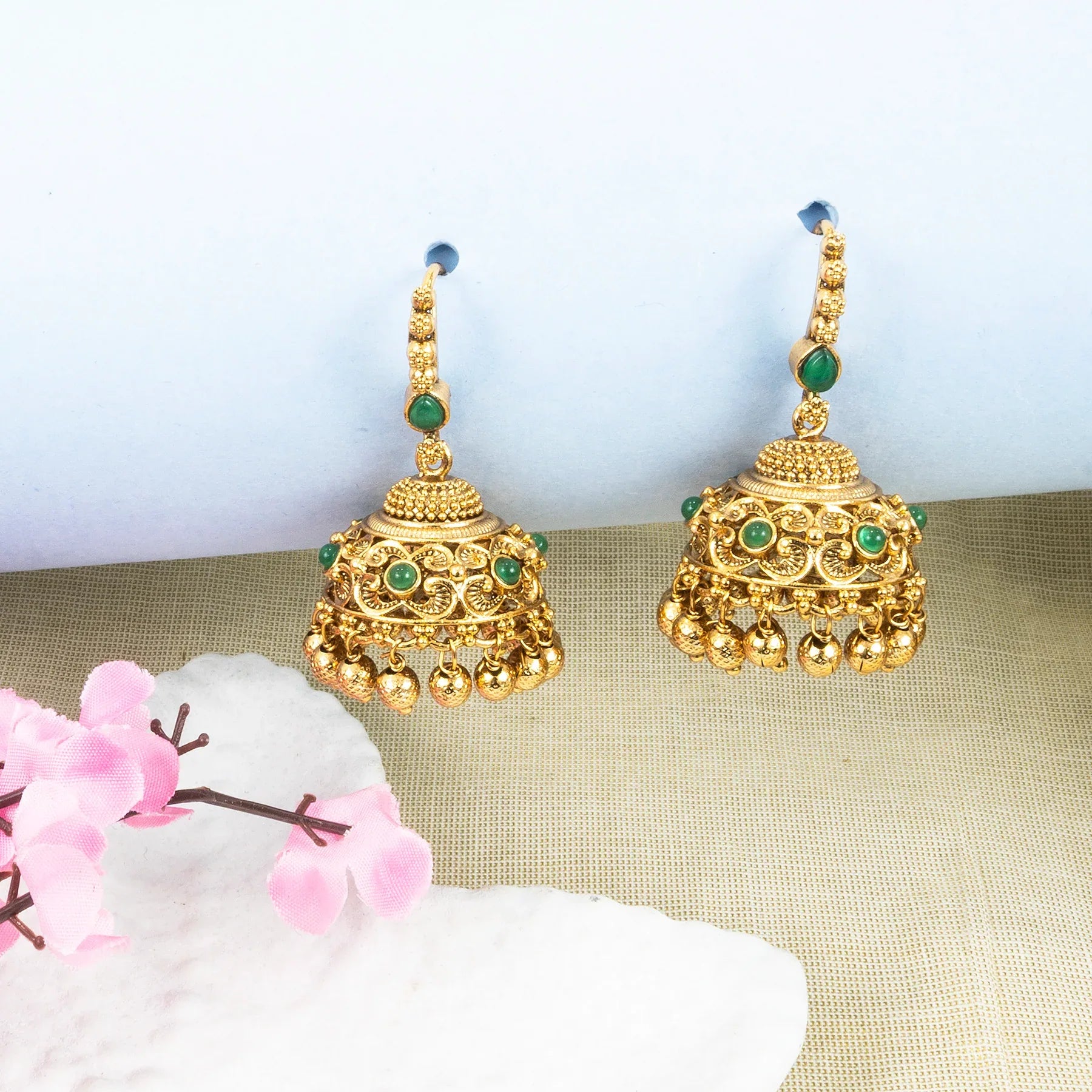 Gold earrings with green gemstones on a beige surface with flowers
