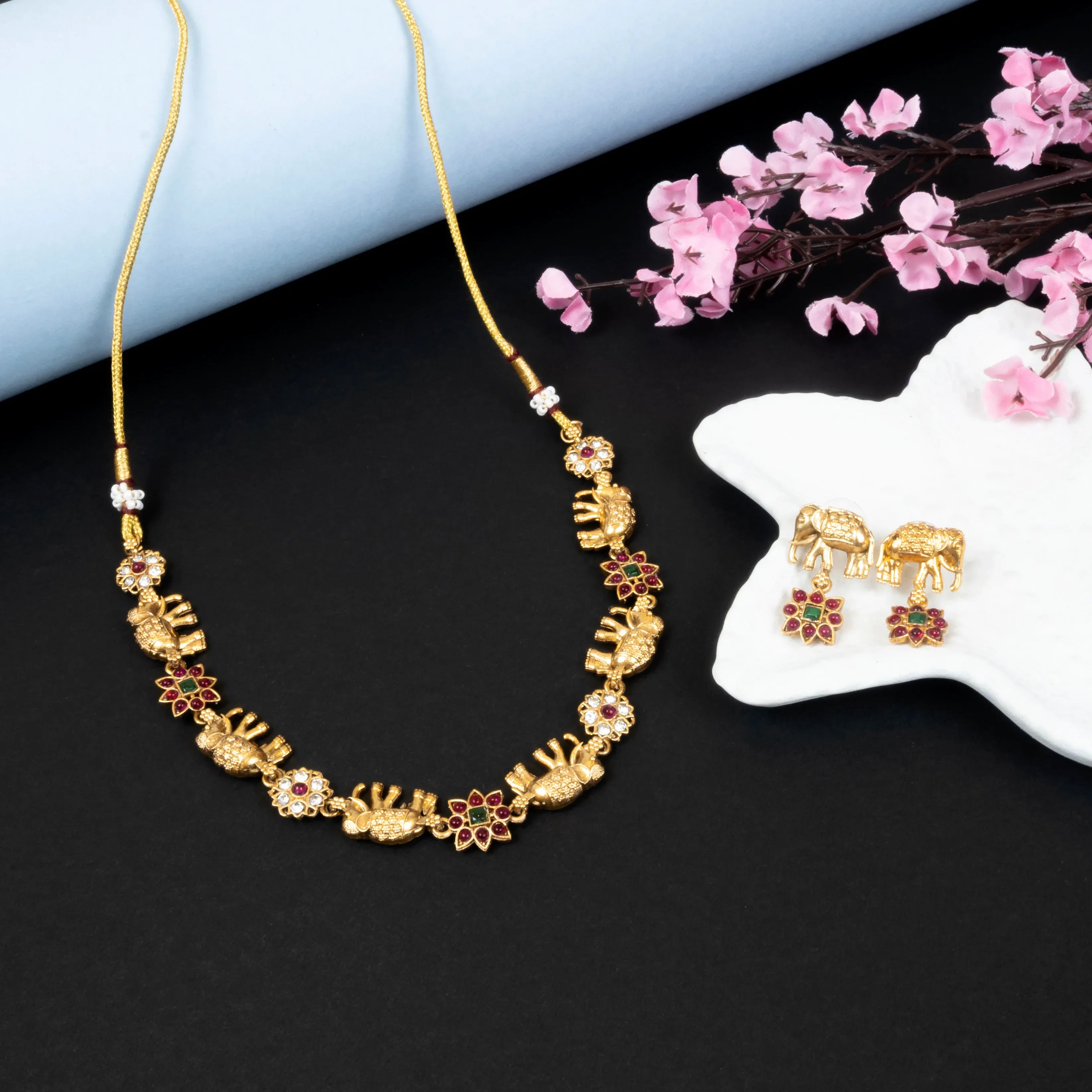 Gold necklace and earrings with floral decorations on a black surface with pink flowers.