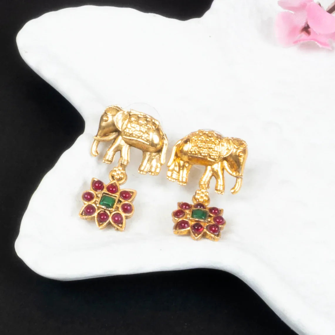 Gold elephant earrings with gemstone accents on a white surface.