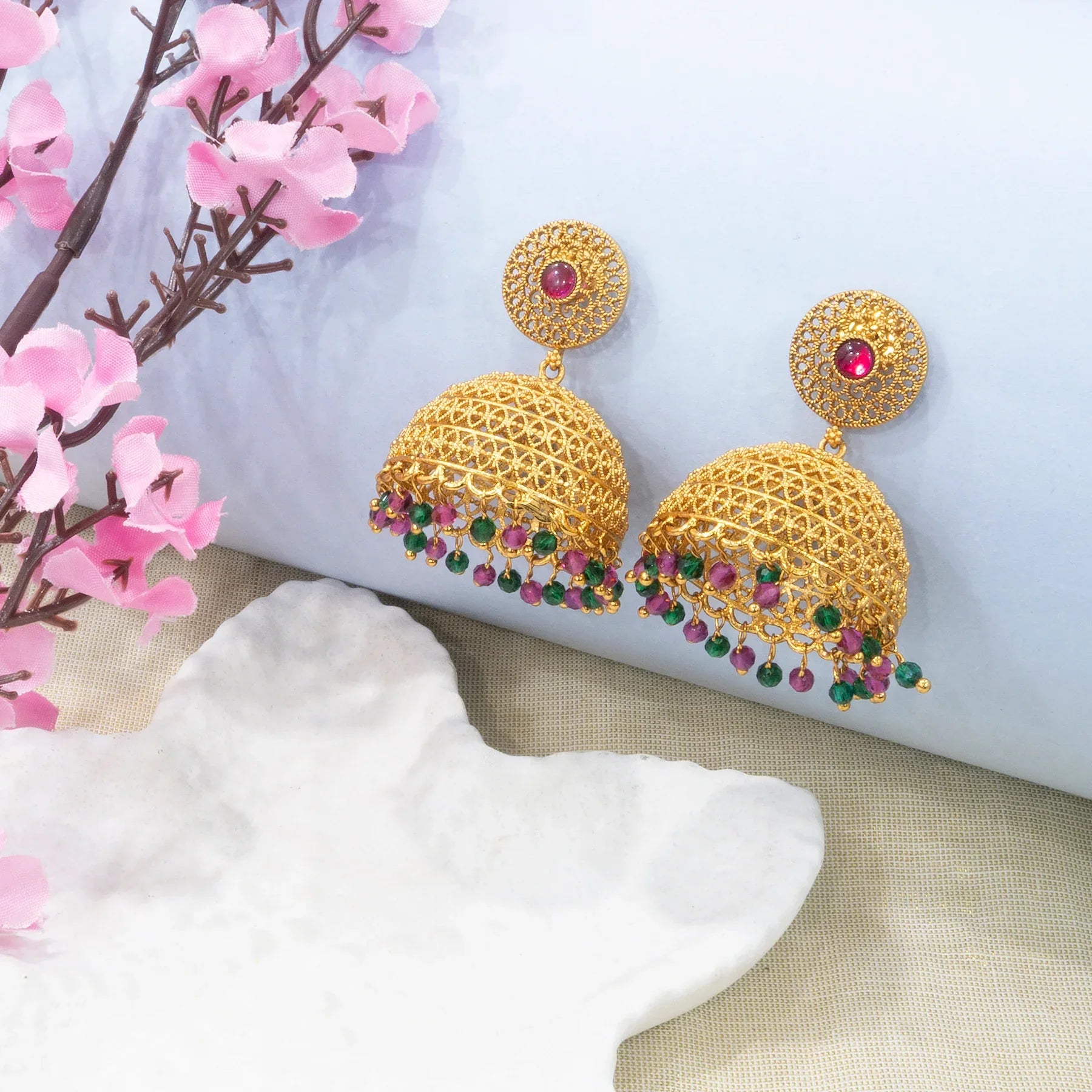 Gold earrings with gemstones on a decorative surface with pink flowers