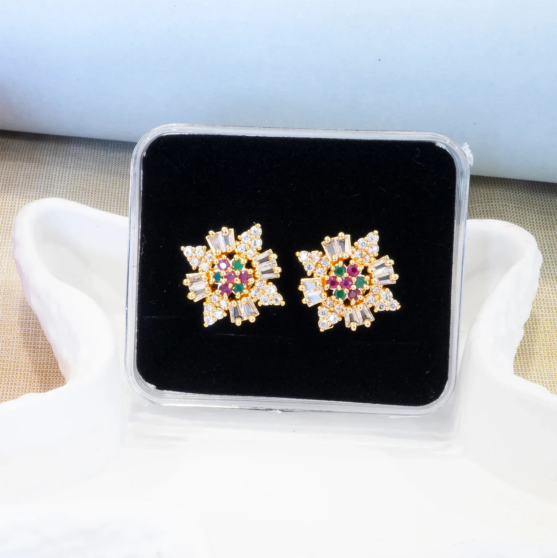 Gold earrings with gemstones on a black display stand against a white background