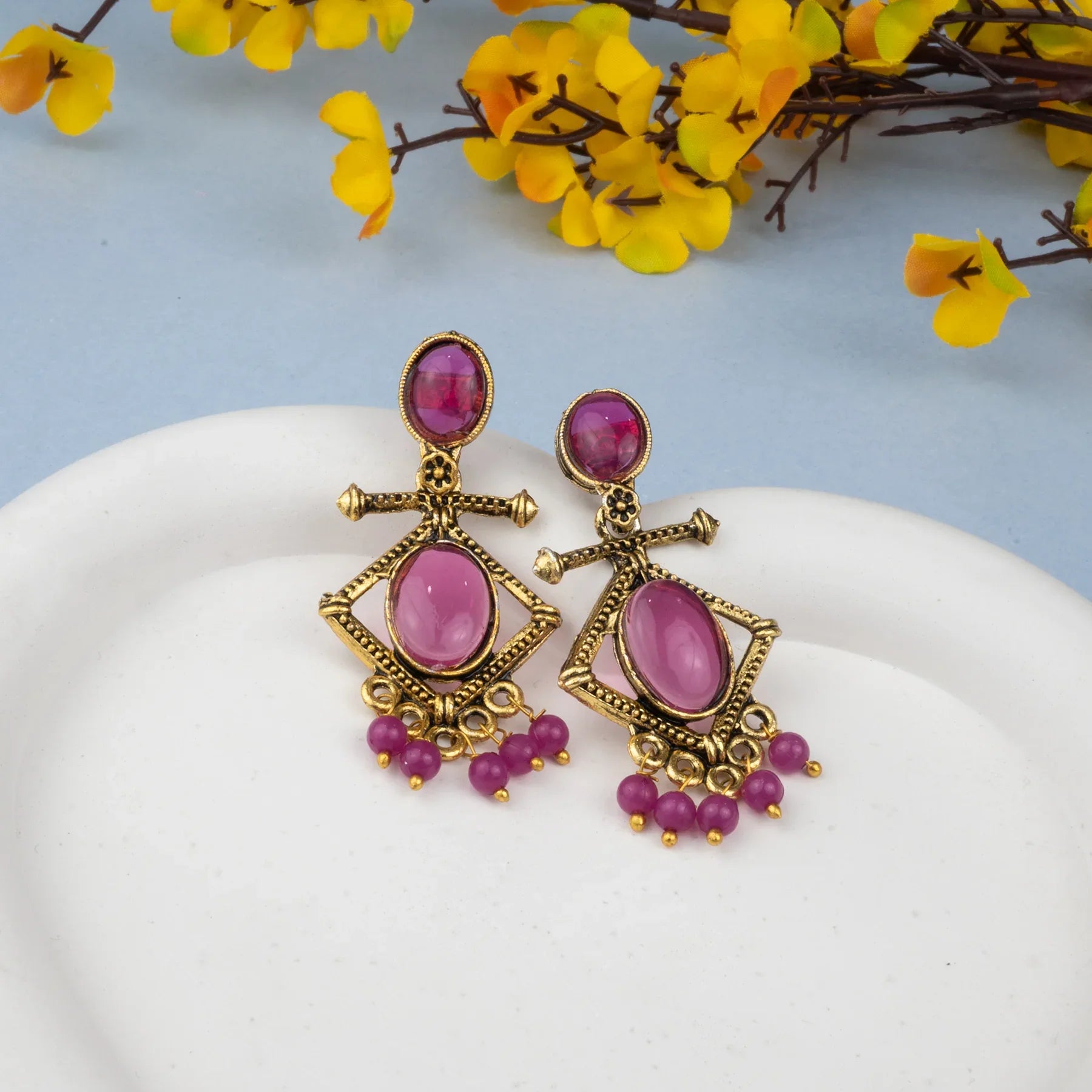 Ornate earrings with pink gemstones on a white plate with yellow flowers in the background