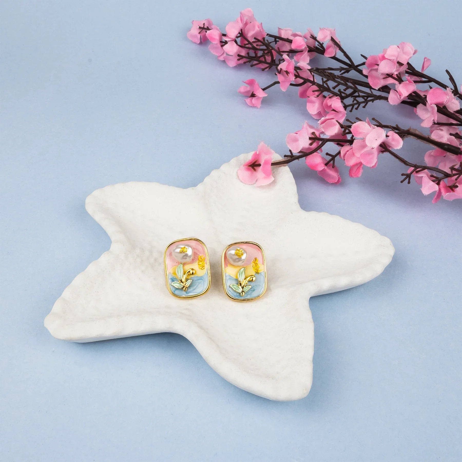 Pair of earrings on a starfish with pink flowers on a light blue background