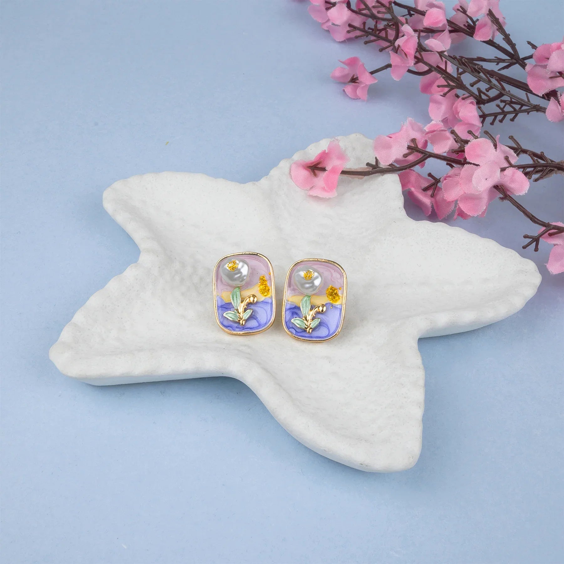 Pair of earrings on a star-shaped stand with pink flowers in the background