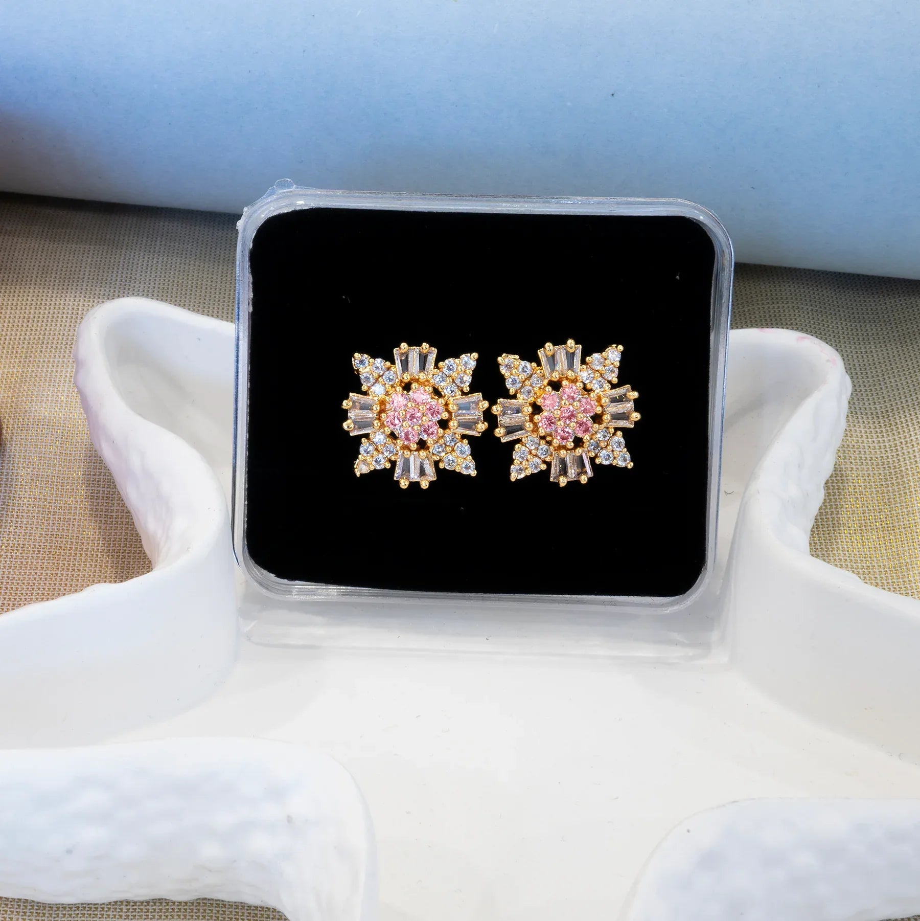 Pair of gold and pink earrings on a black display card held by white gloves.