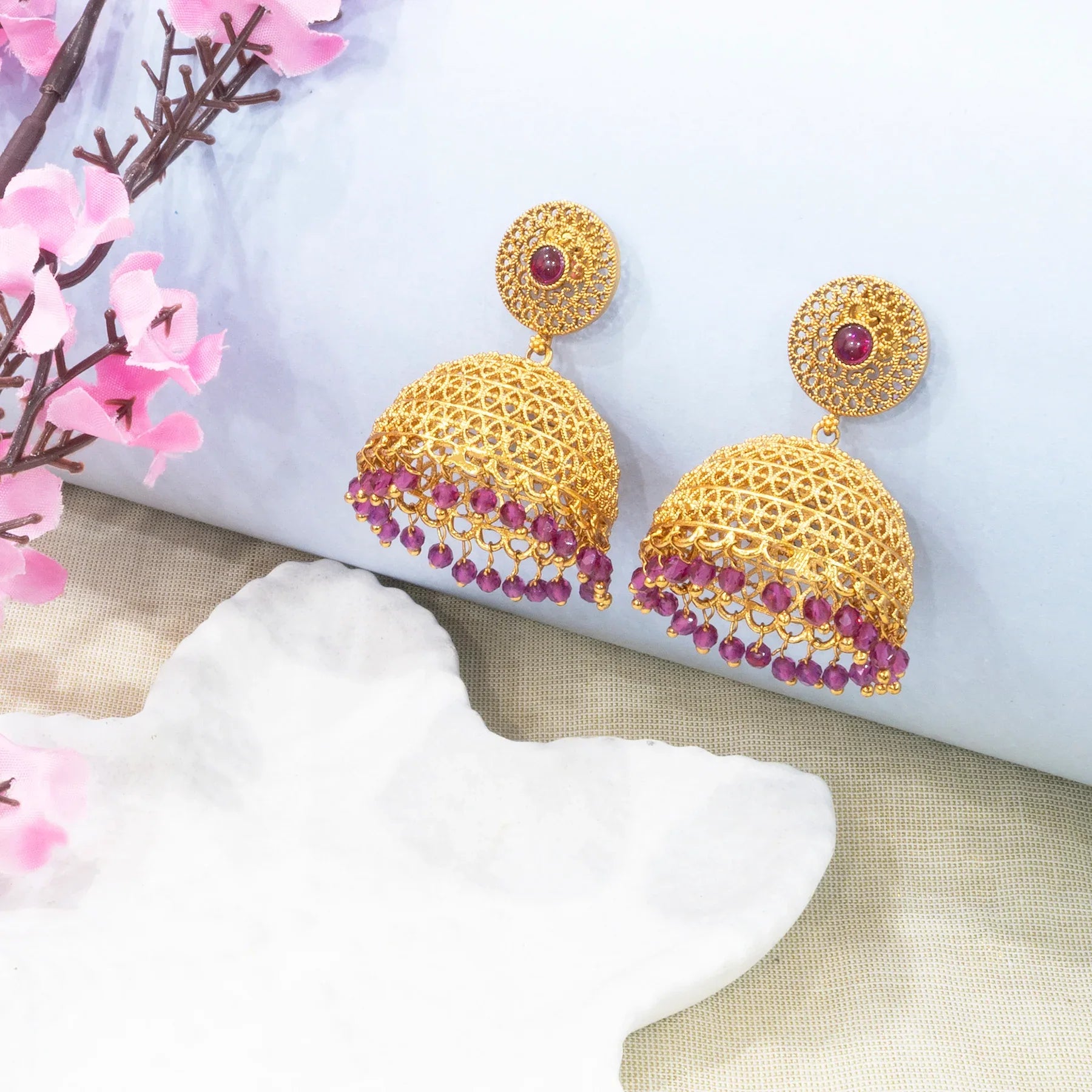 Gold earrings with red gemstones on a white surface with pink flowers.