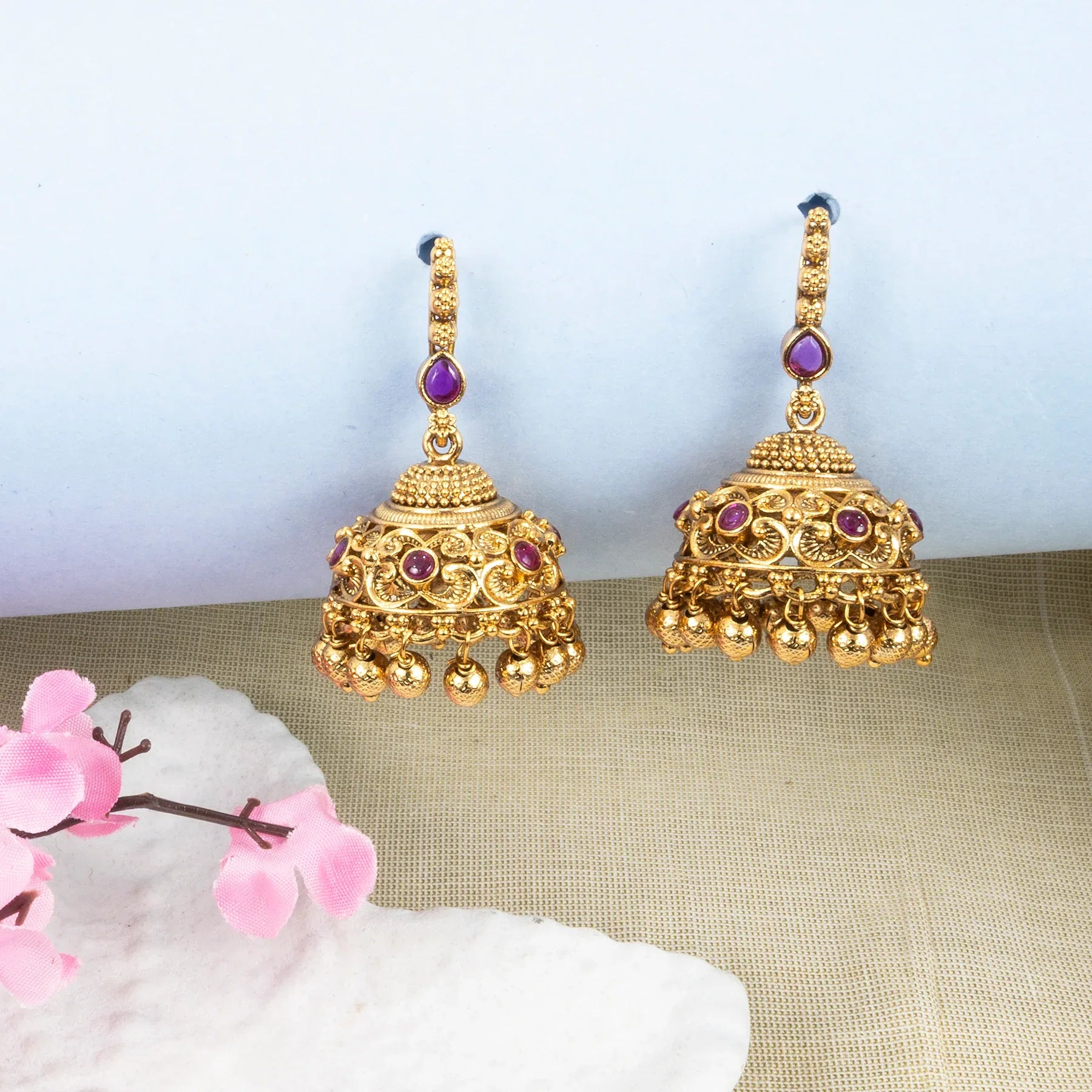 Gold earrings with purple gemstones on a light background