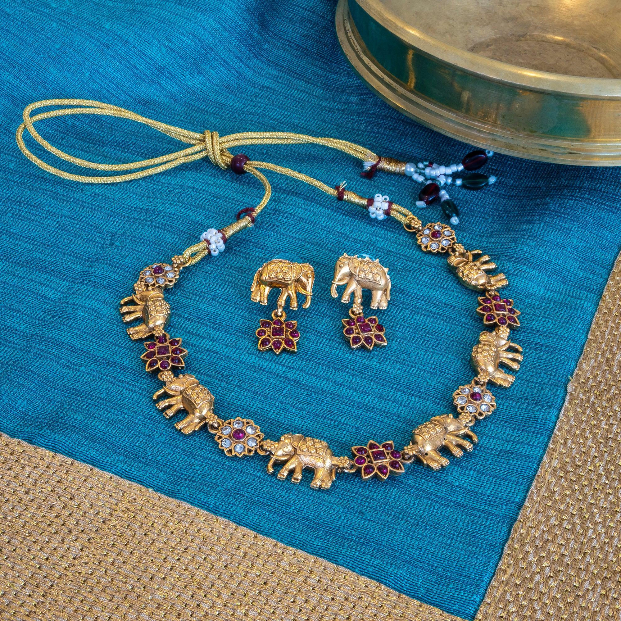 Gold elephant-themed necklace and earrings on a blue fabric background