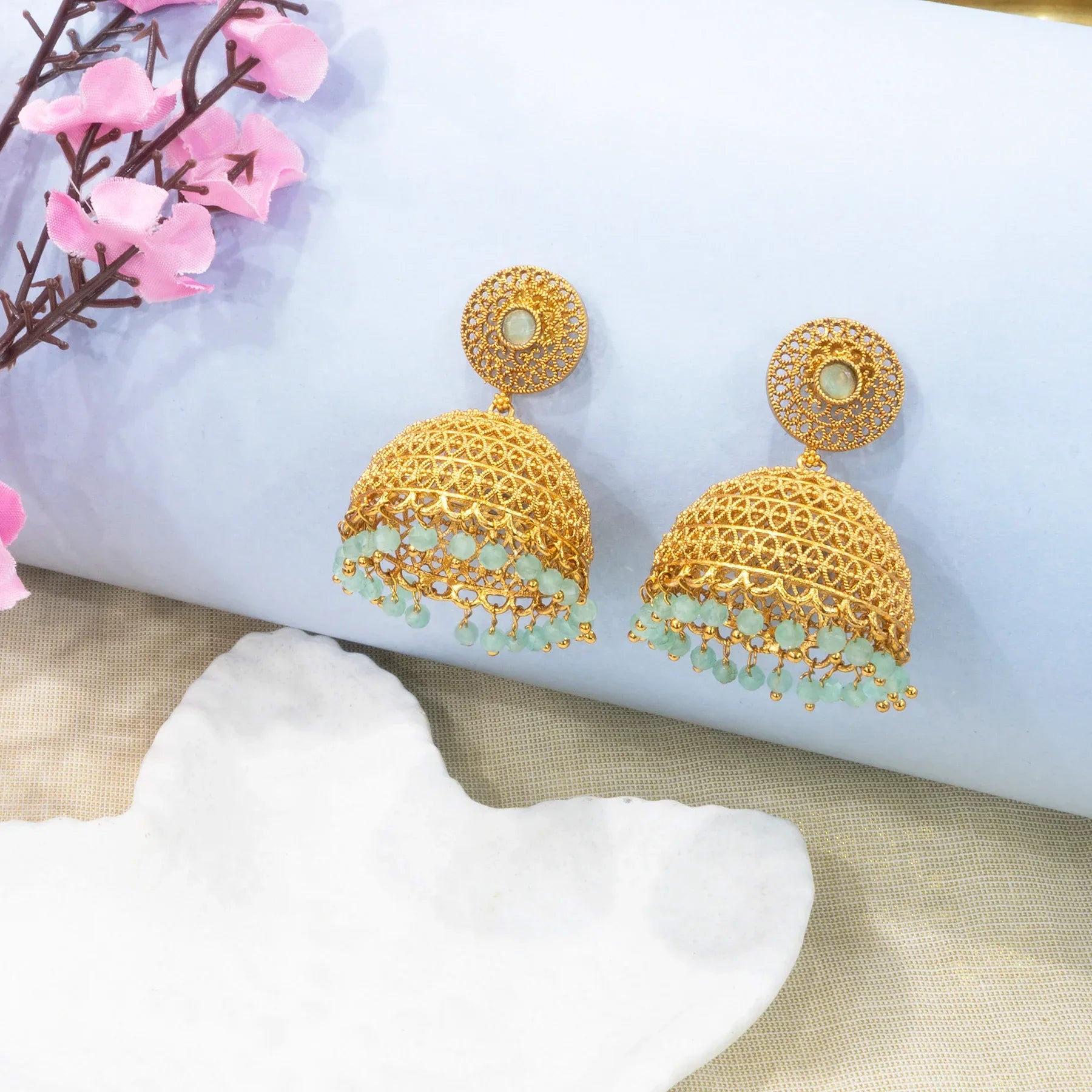 Gold earrings with green stones on a decorative surface with flowers.