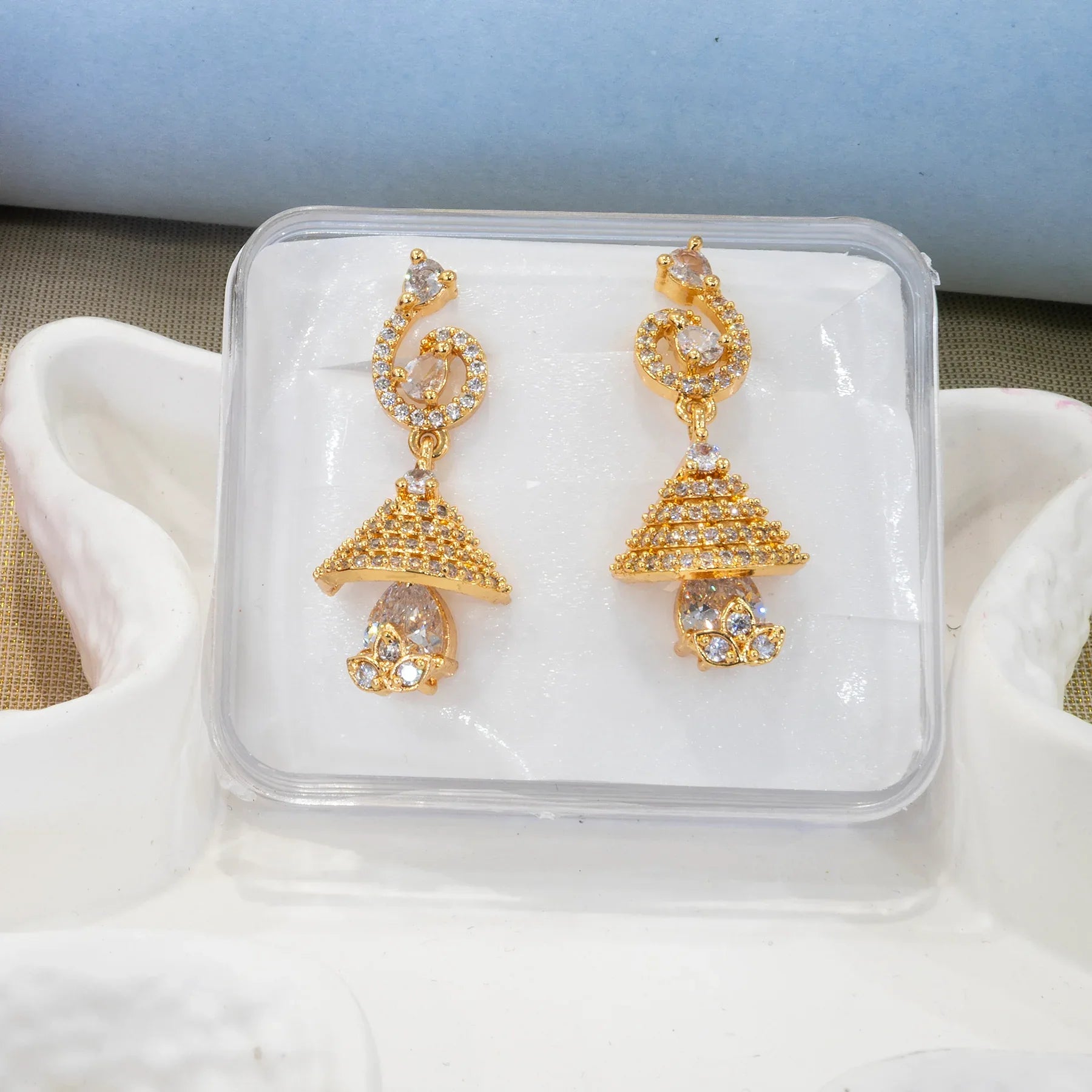 Gold earrings with clear stones in a clear jewelry box on a white surface.