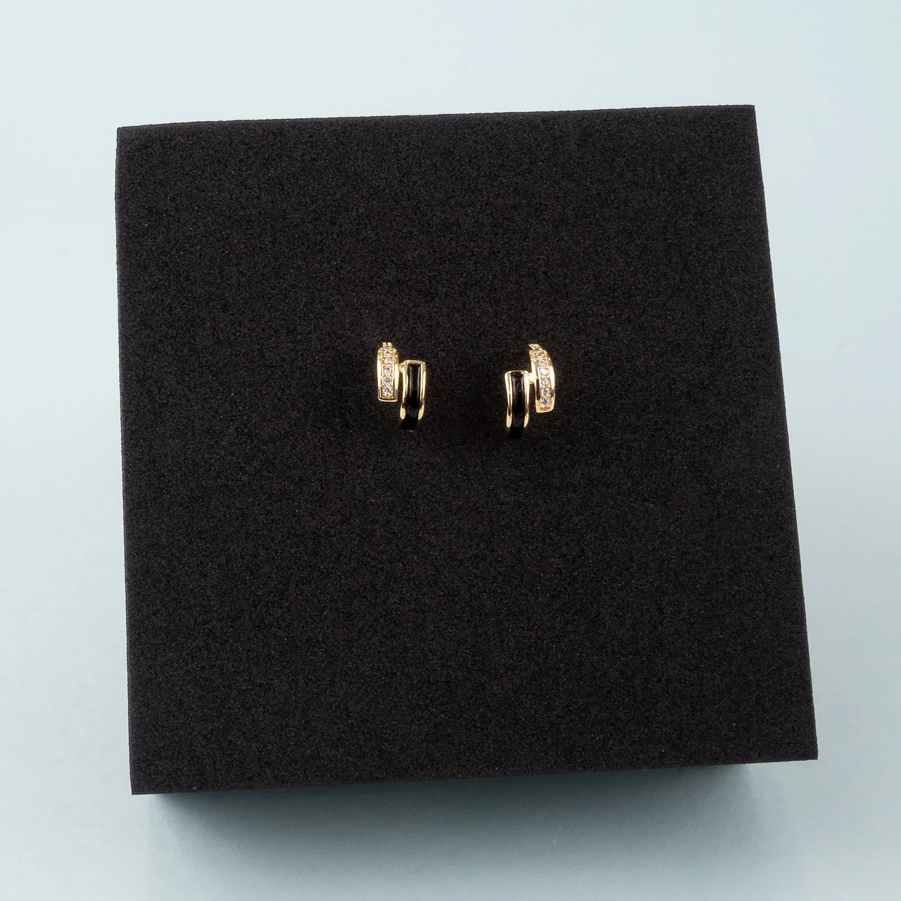 Gold earrings on a black square pad against a light gray background