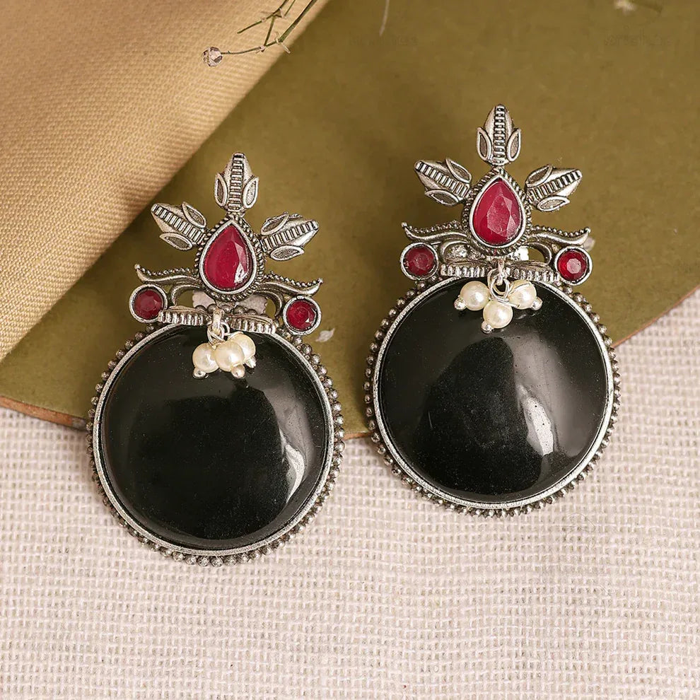 Pair of black stone earrings with silver and red accents on a textured surface