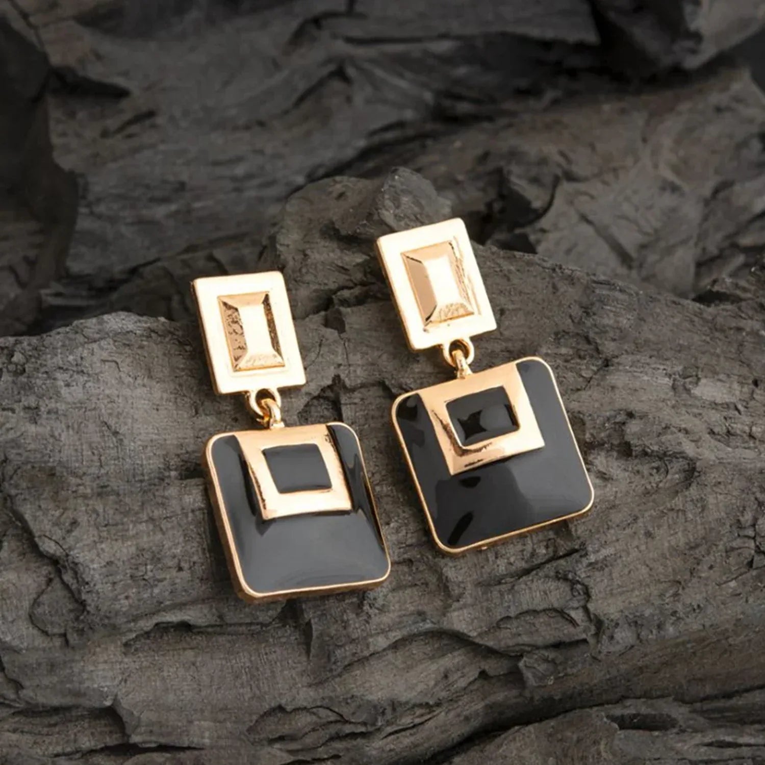 Gold and black square earrings on a dark stone surface