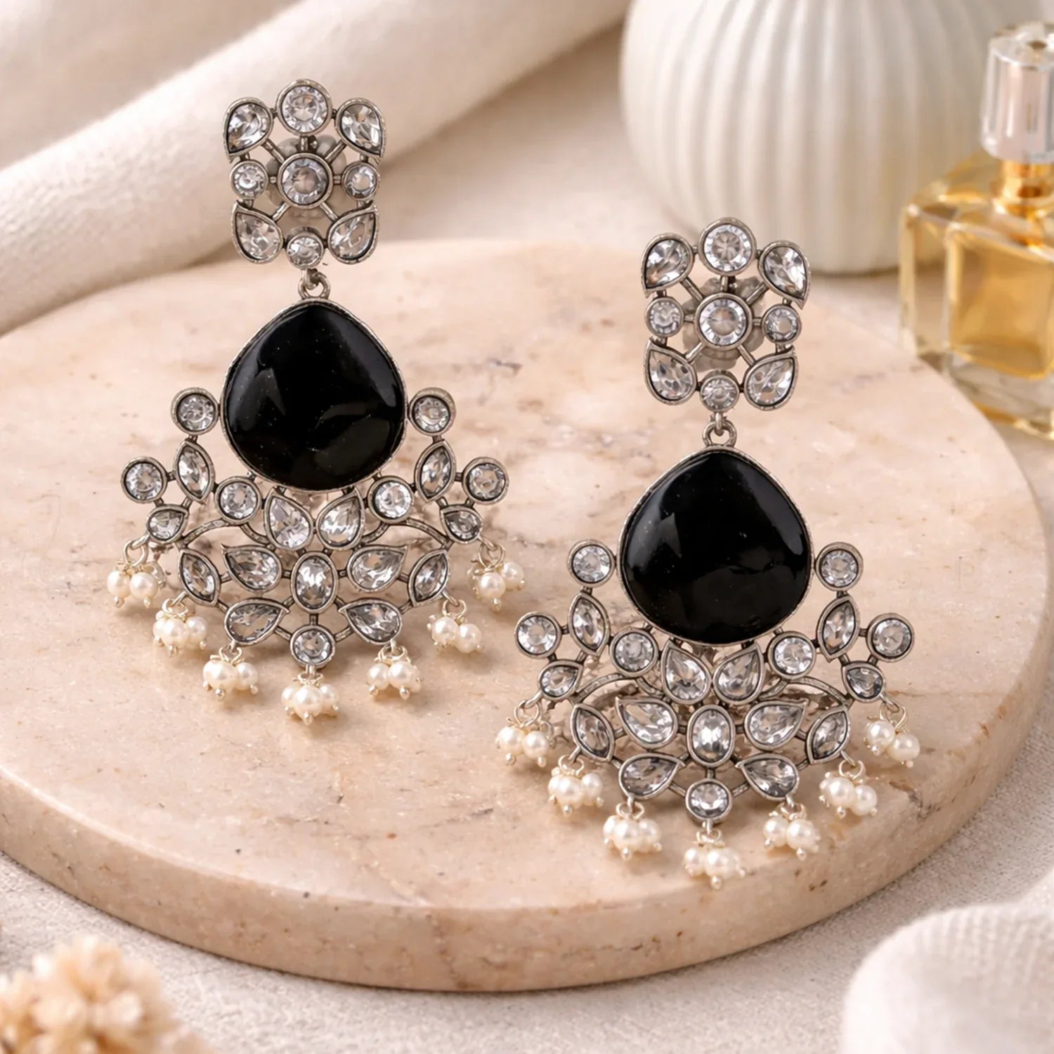 Pair of ornate earrings with black stones and pearl-like elements on a stone surface.