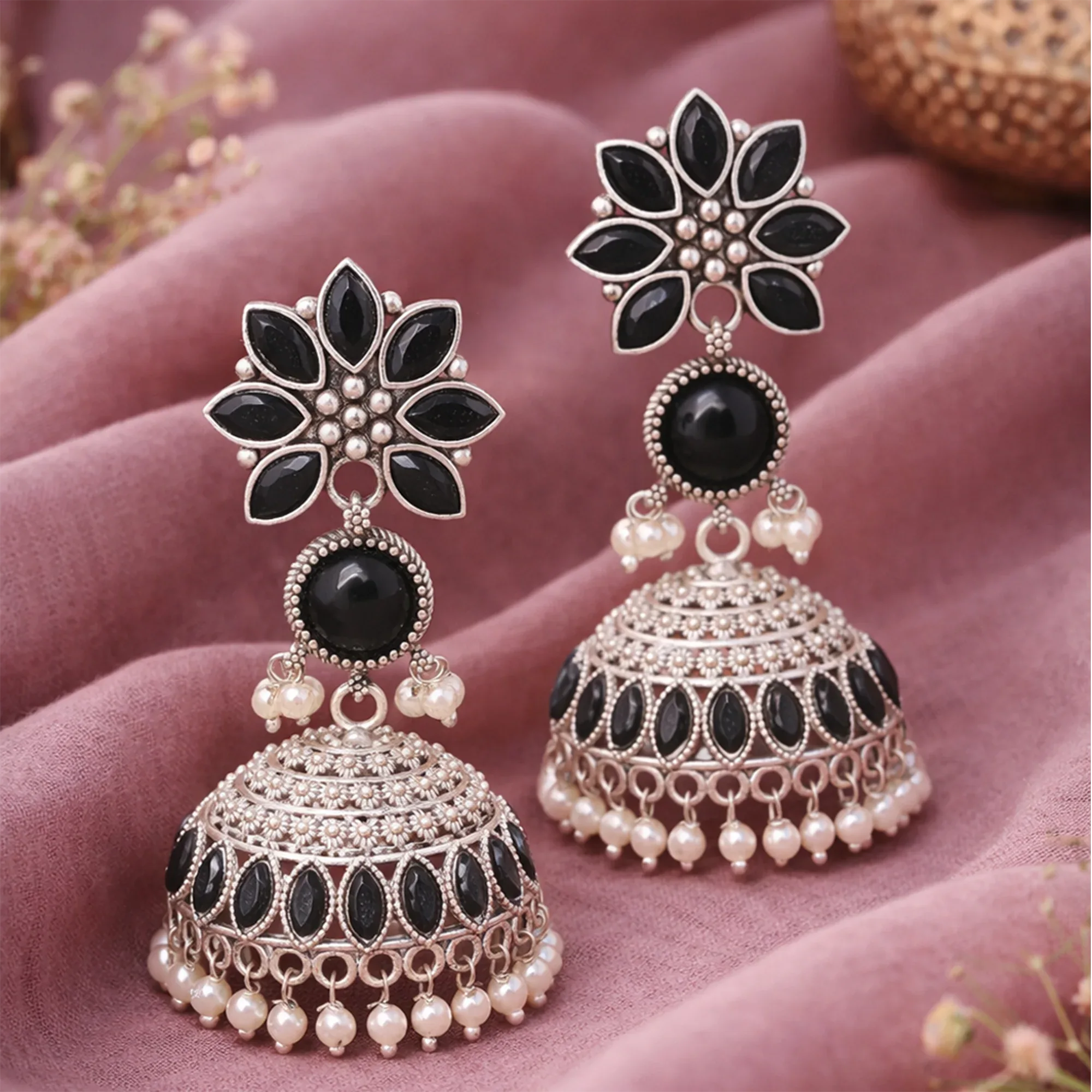 Ornate earrings with black and white stones on a pink fabric background