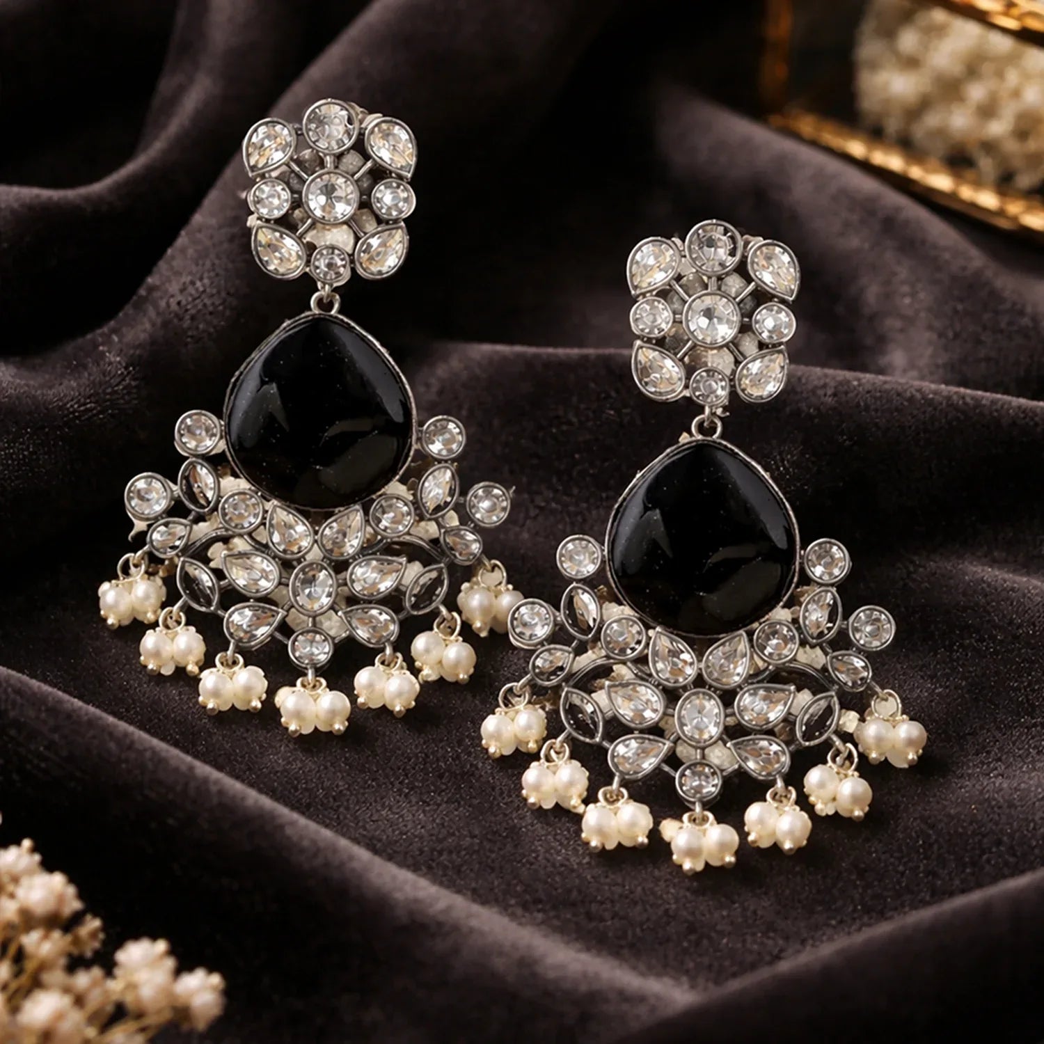 Ornate earrings with black stones and pearl-like elements on a dark fabric background