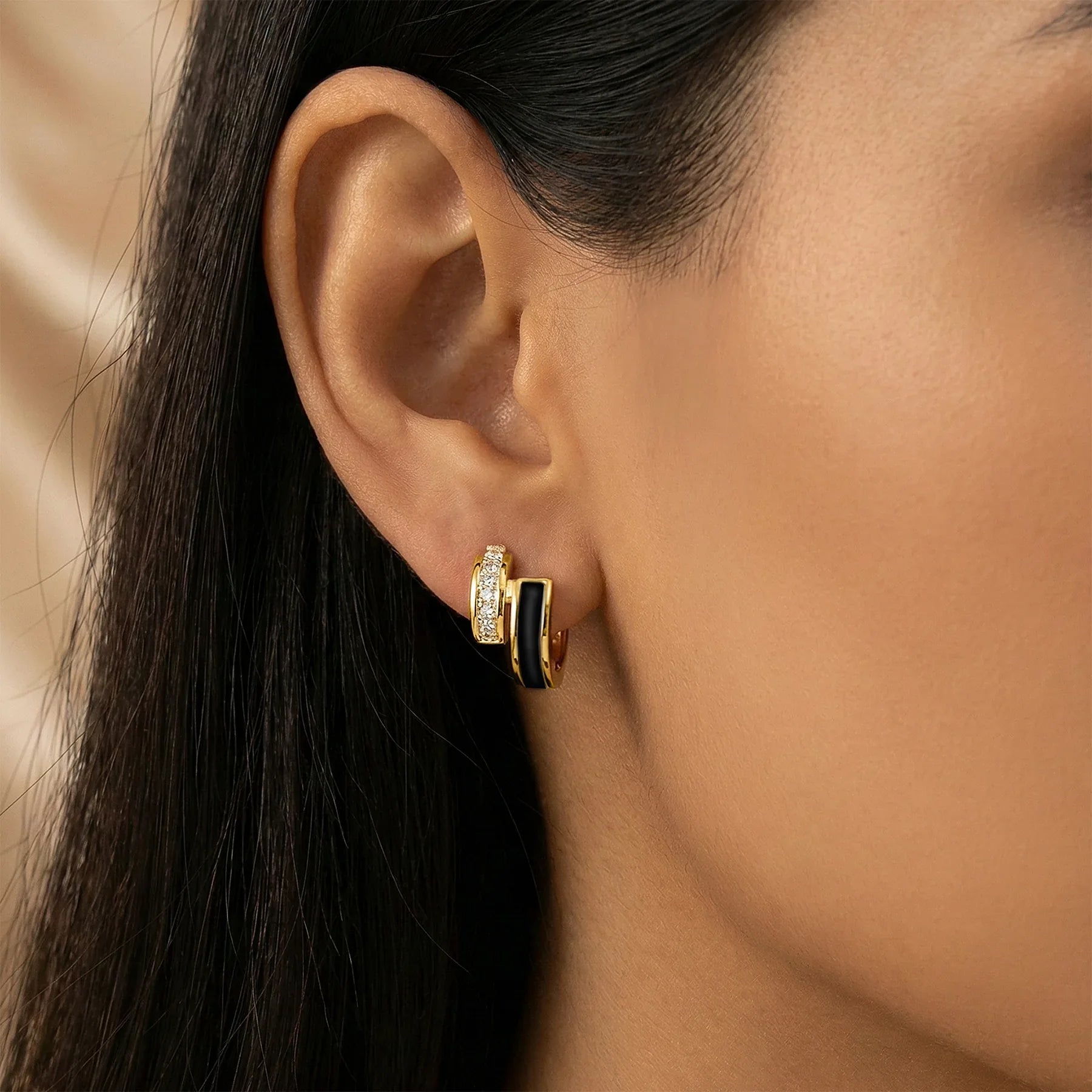 Close-up of an ear wearing a gold and black hoop earring.