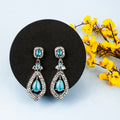 Teal teardrop earrings on a black stand with yellow flowers in the background