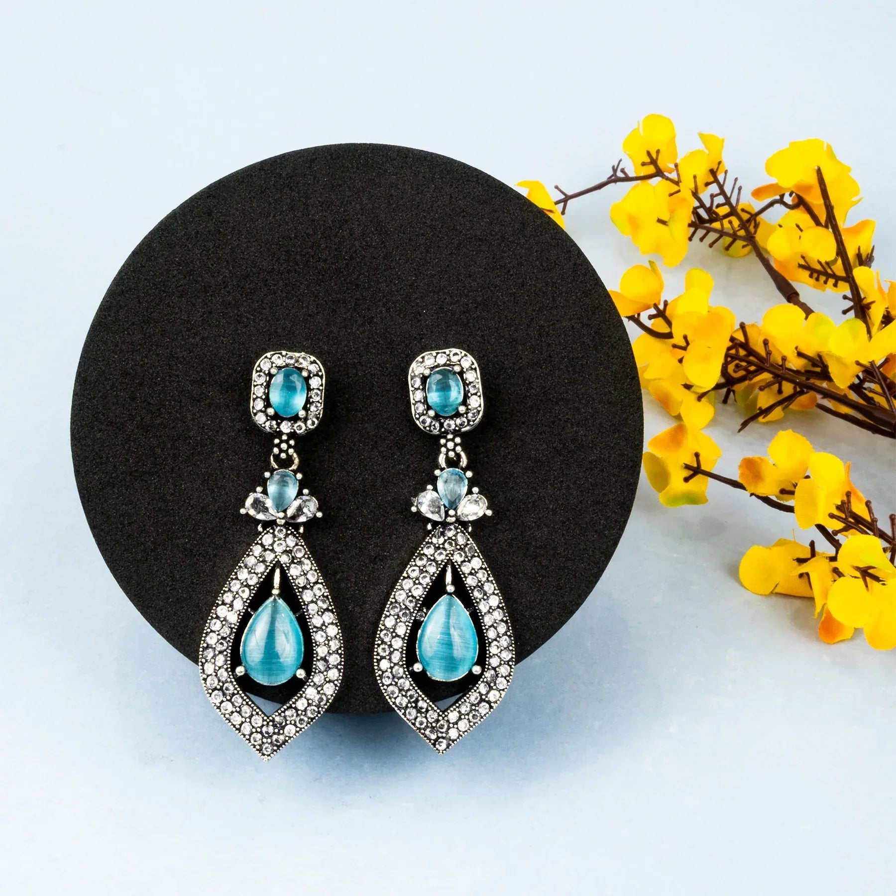 Teal teardrop earrings on a black stand with yellow flowers in the background