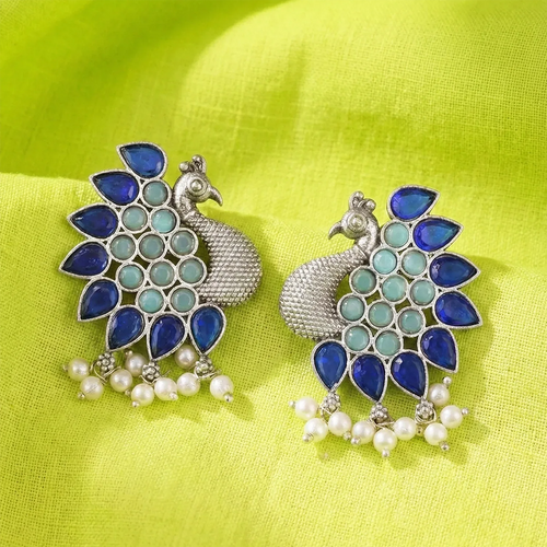 Pair of peacock-shaped earrings with blue and green stones on a bright green fabric background
