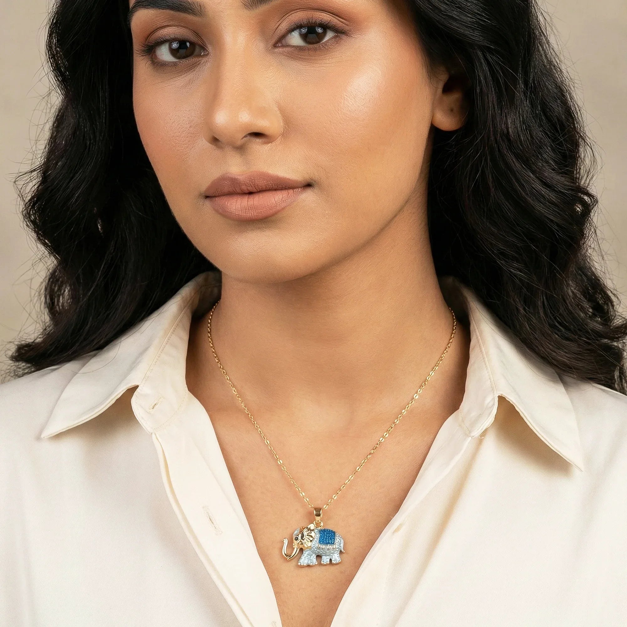 Woman wearing a gold necklace with an elephant pendant against a neutral background