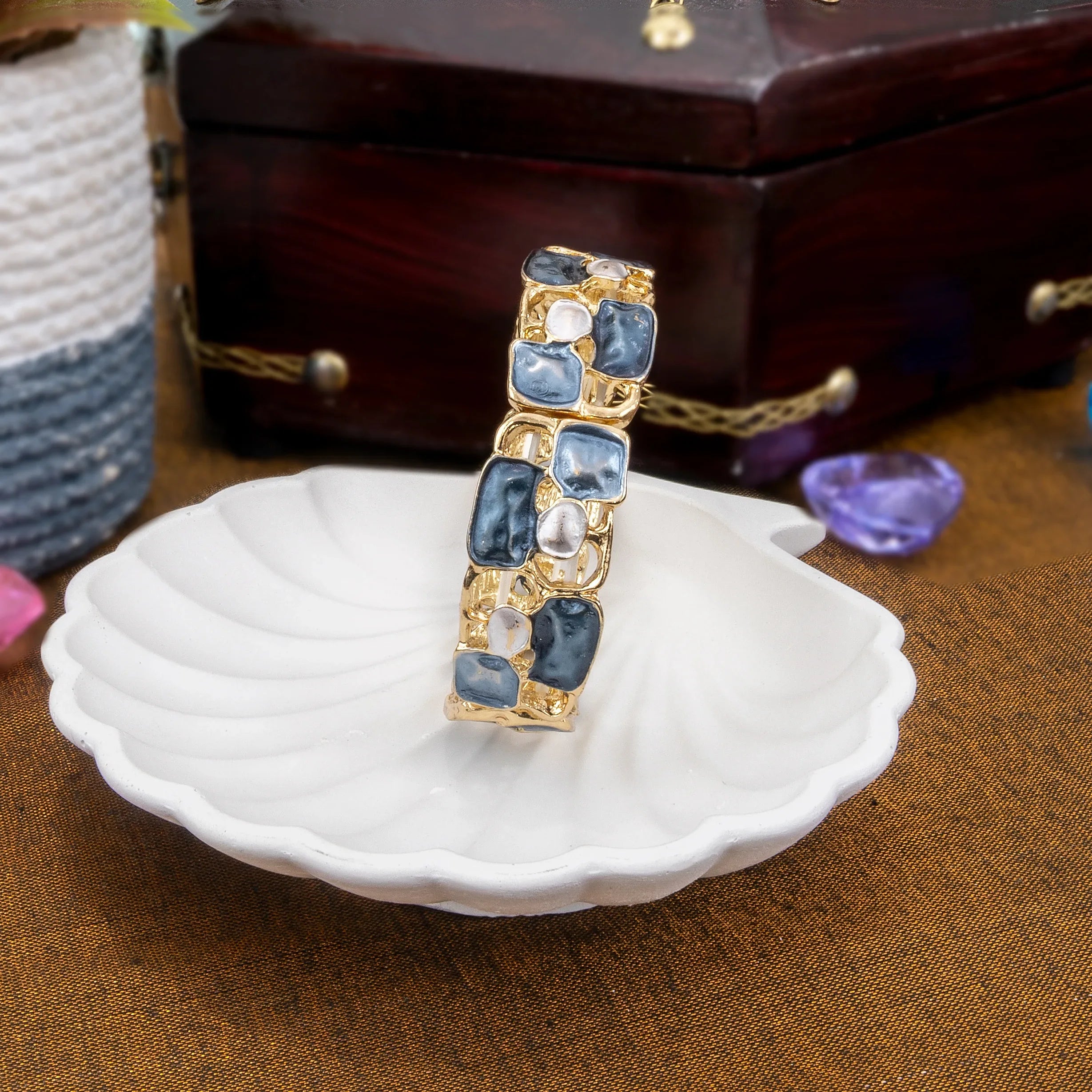 Gold bracelet with blue stones on a white dish with a wooden box in the background